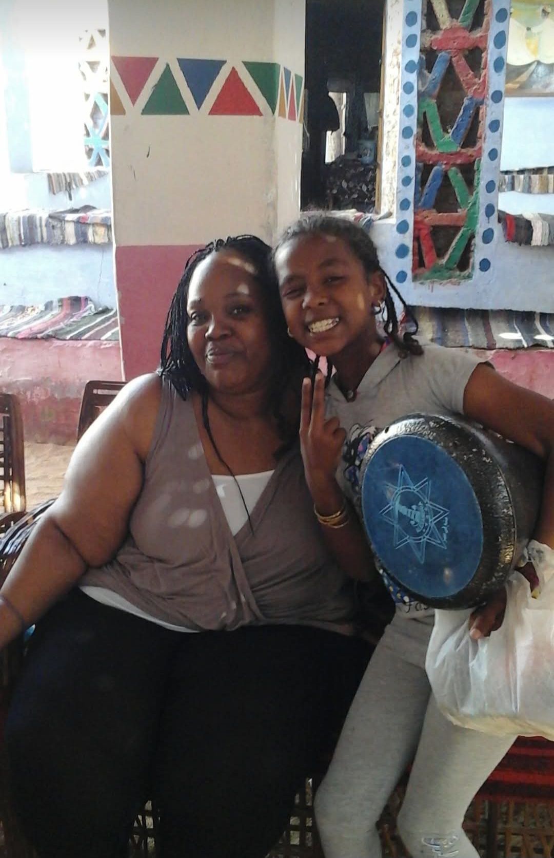 Two women posing for a picture with one holding a drum