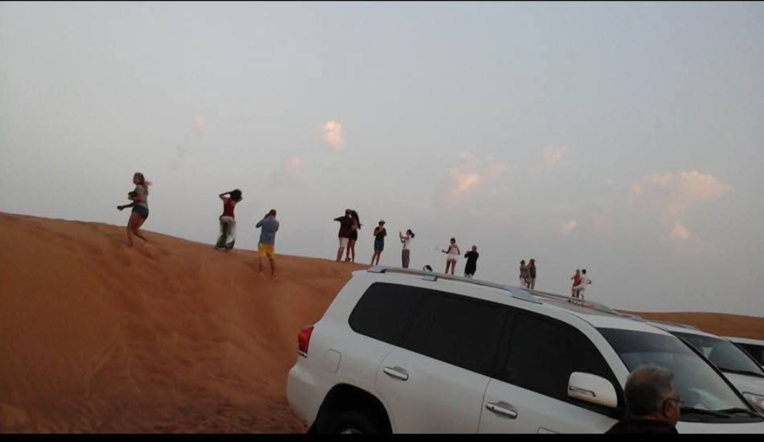 A group of people standing on top of a sand dune next to a white suv