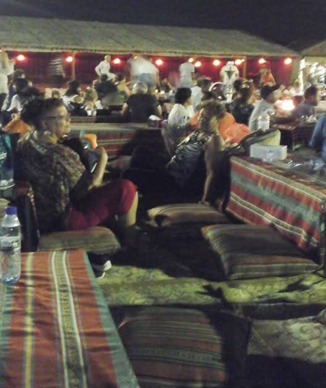 A woman sits at a table with a bottle of water in front of her