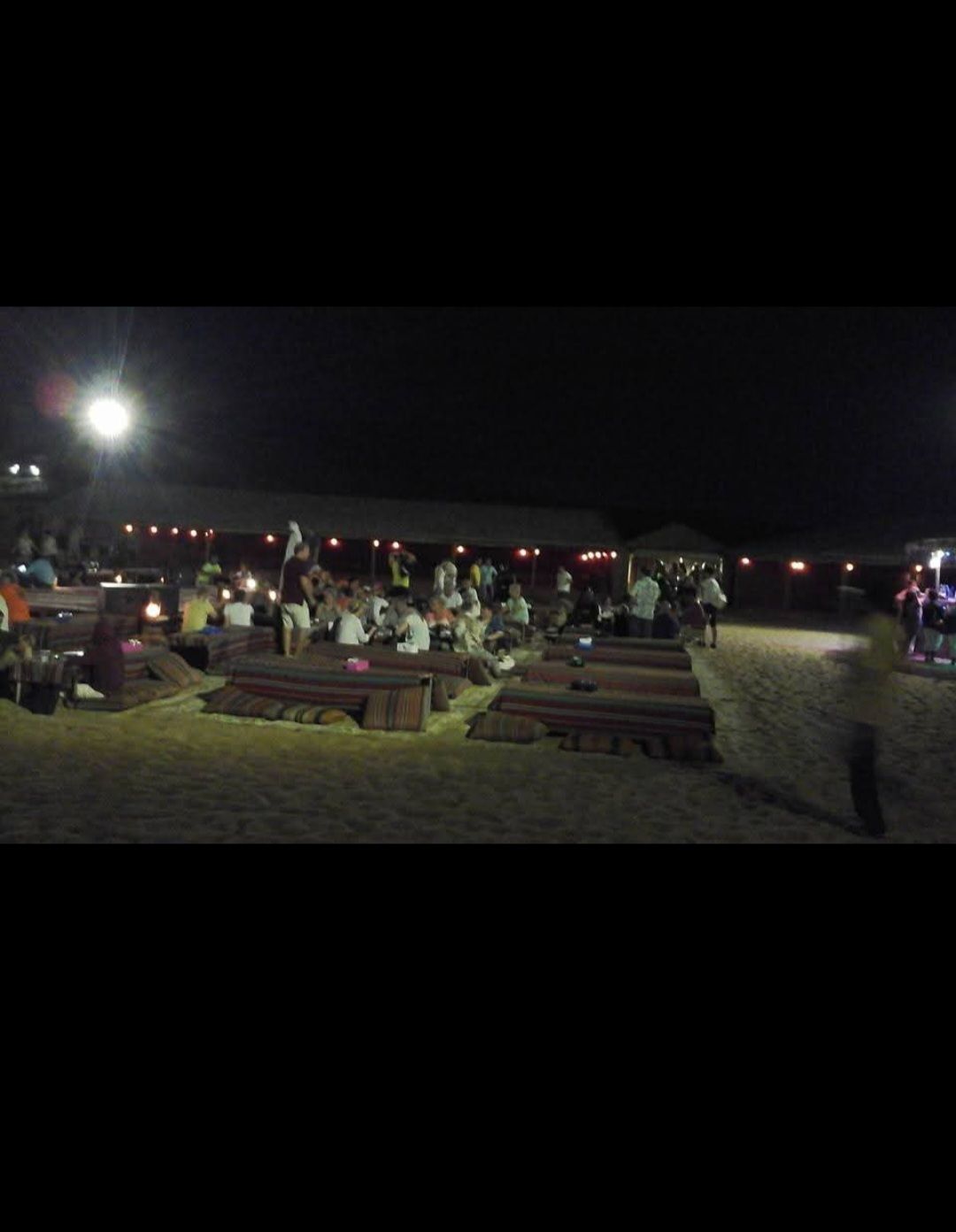 A group of people sitting at picnic tables under a tent at night