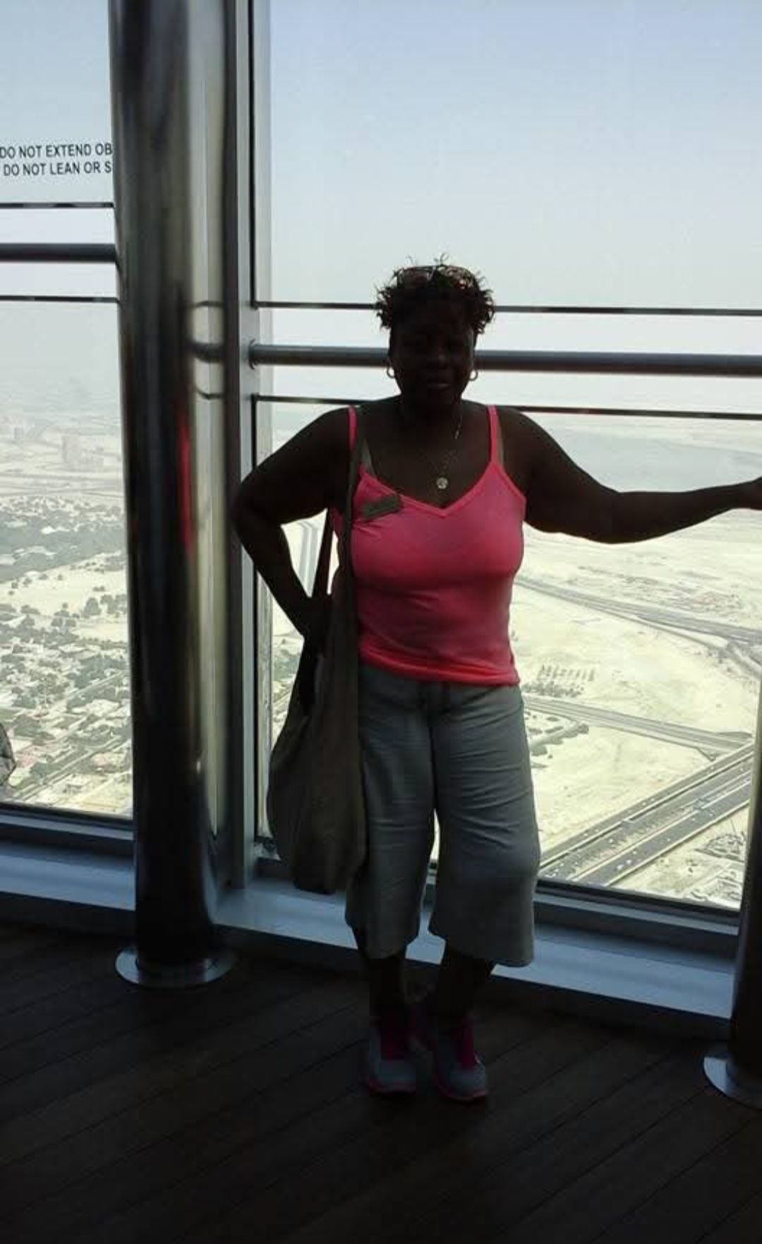 A woman in a pink tank top is standing in front of a window.