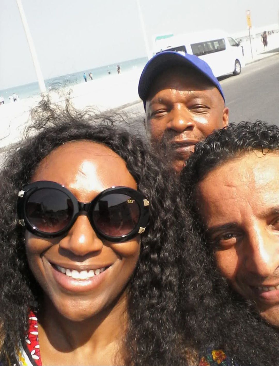 A woman wearing sunglasses poses for a selfie with two men