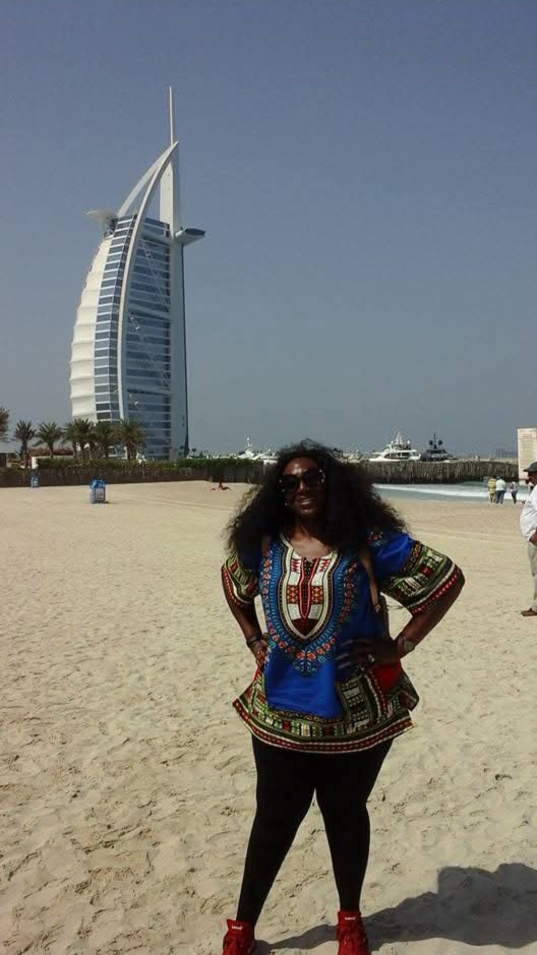 A woman is standing on a beach in front of a large building.