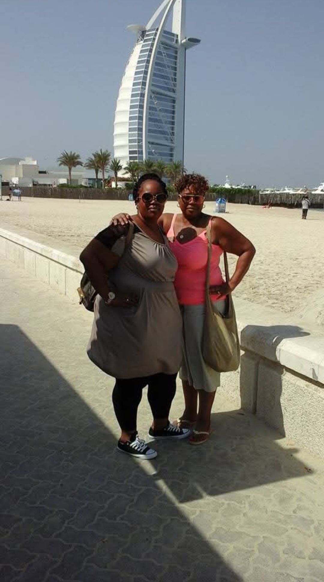 Two women are standing next to each other on a beach in front of a building.