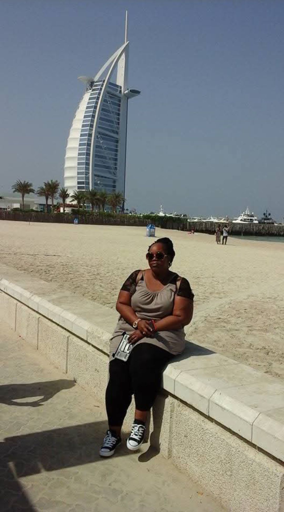 A woman is sitting on a wall in front of a large building.