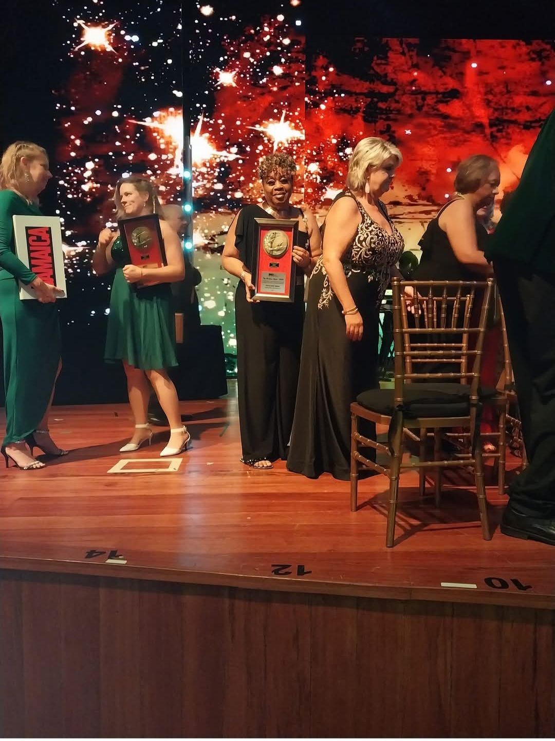 A group of women are standing on a stage holding trophies and one of them is holding a sign that says fame