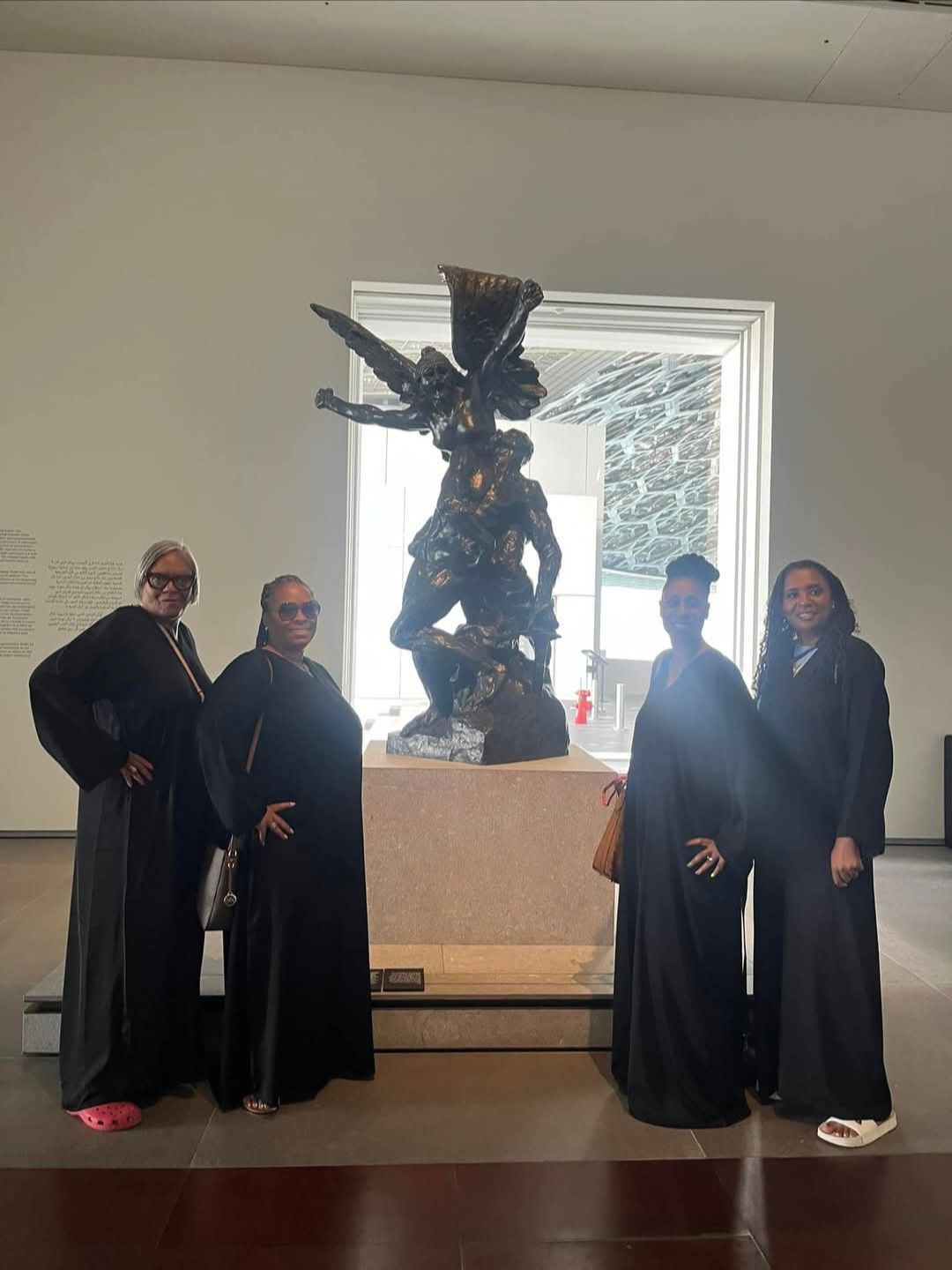 A group of women are standing in front of a statue in a museum.