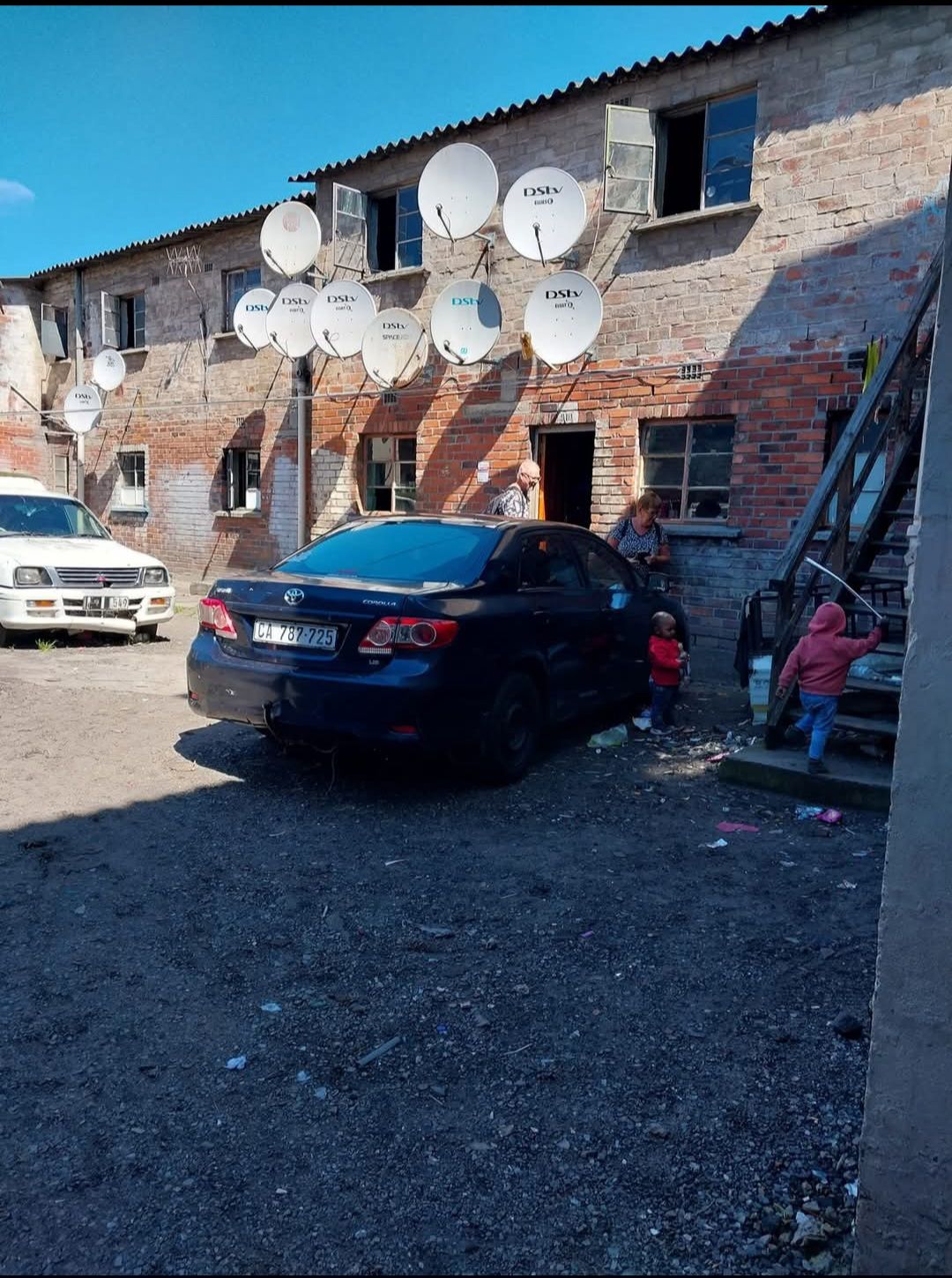 A car is parked in front of a building with satellite dishes on the side