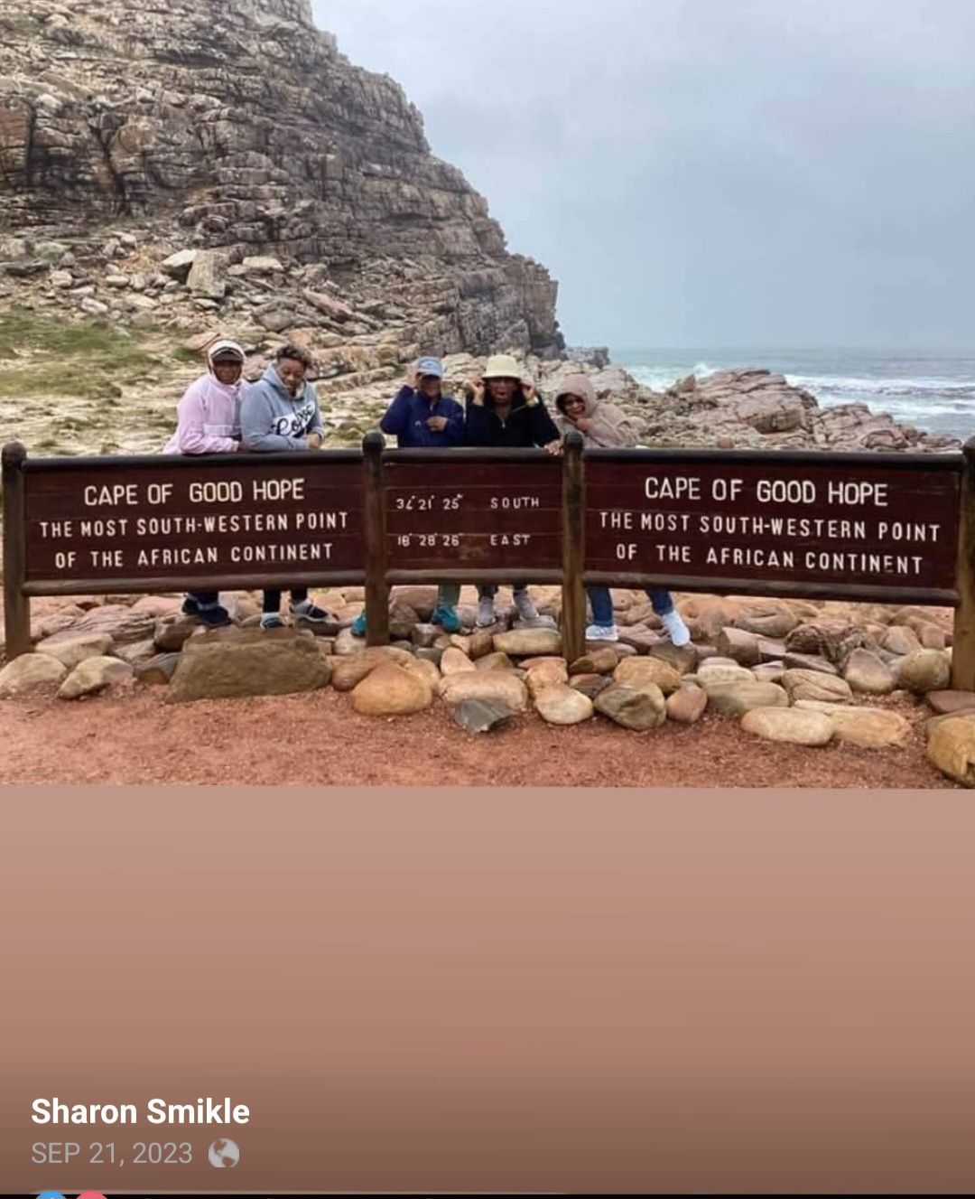 A group of people standing in front of a sign that says cape of good hope.