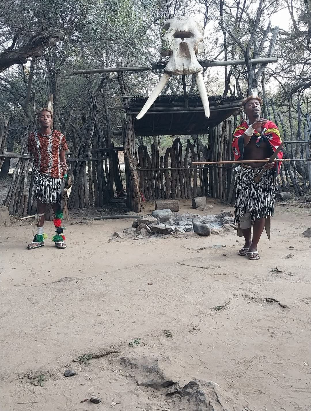 Two people are standing in the dirt in front of a skeleton.