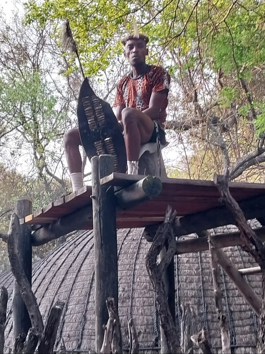 A man is sitting on top of a wooden structure in the woods.