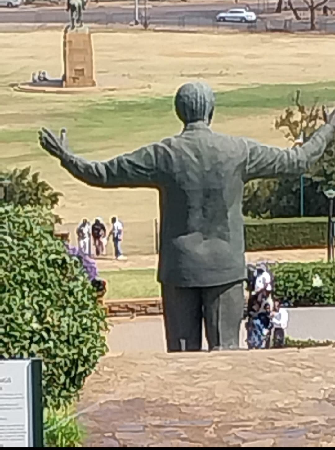 A statue of nelson mandela is standing in a park with his arms outstretched.