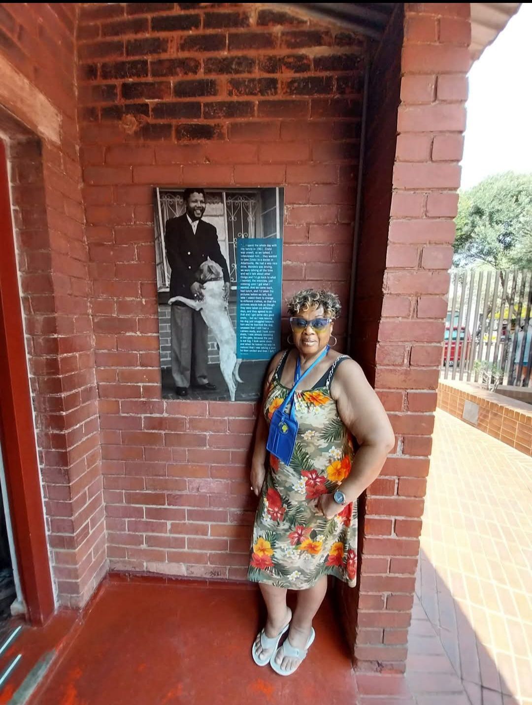 A woman in a floral dress is standing in front of a brick wall