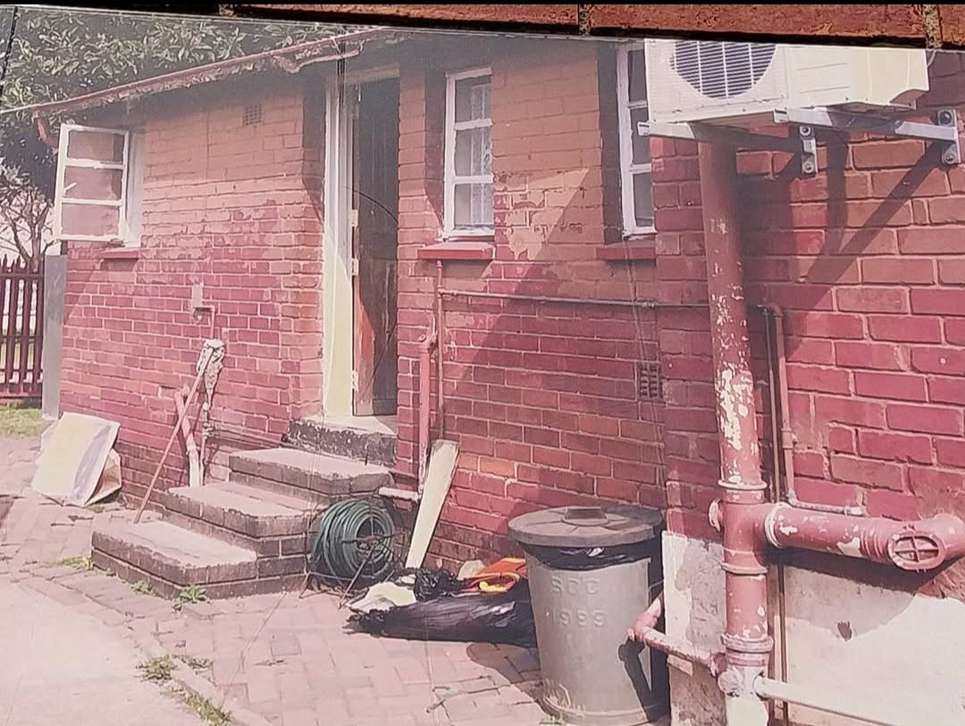 A brick house with stairs and a trash can in front of it.