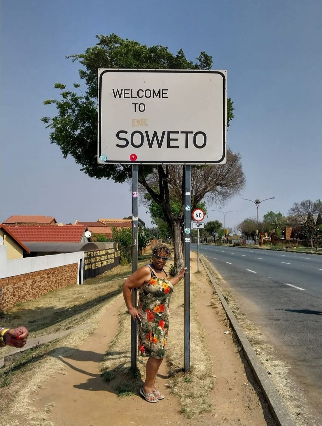 A woman stands in front of a sign that says welcome to soweto