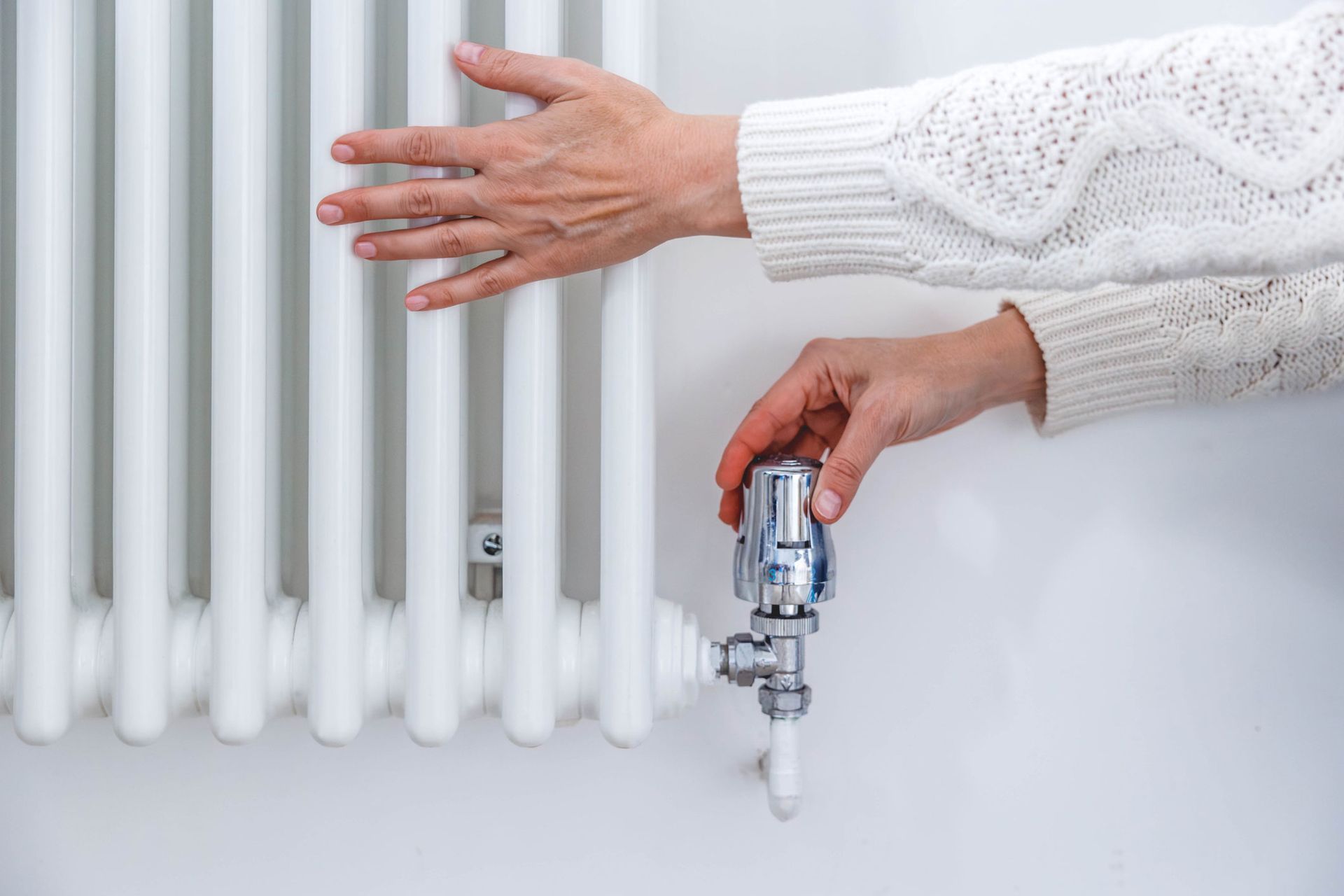 A person is adjusting the temperature of a radiator with their hands.