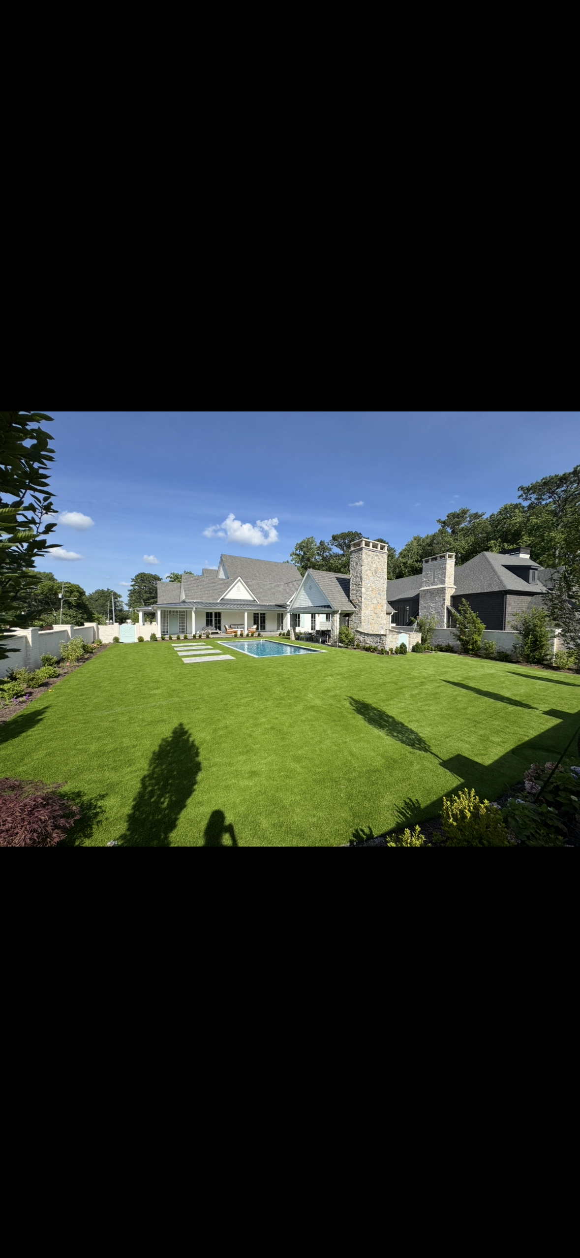 Large house with a green lawn, trees, and a blue sky.