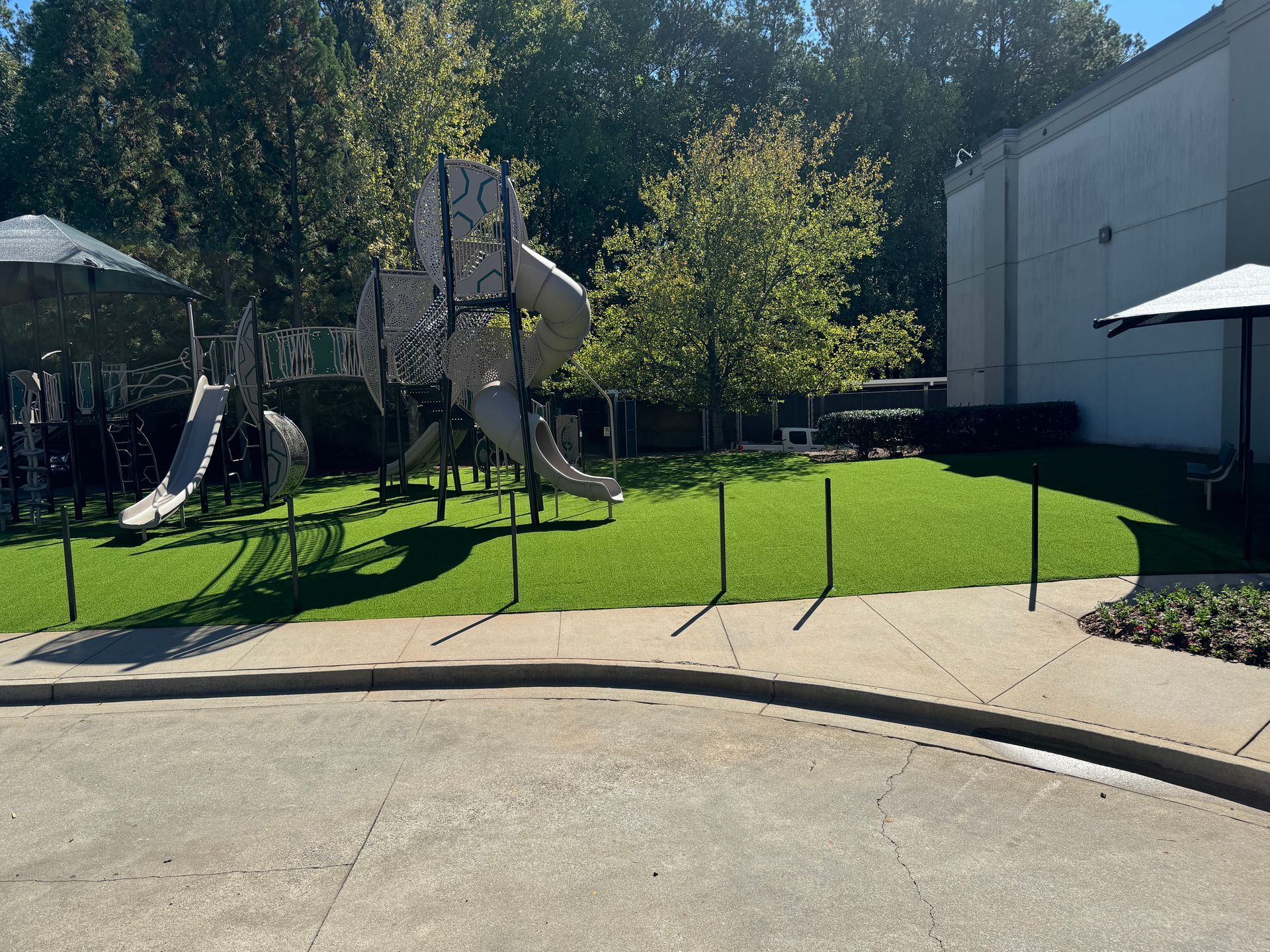 Playground with slides and climbing structures on green turf, beside a building and trees.