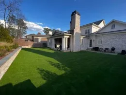 Backyard of a house with a lush green lawn, brick chimney, and clear blue sky.