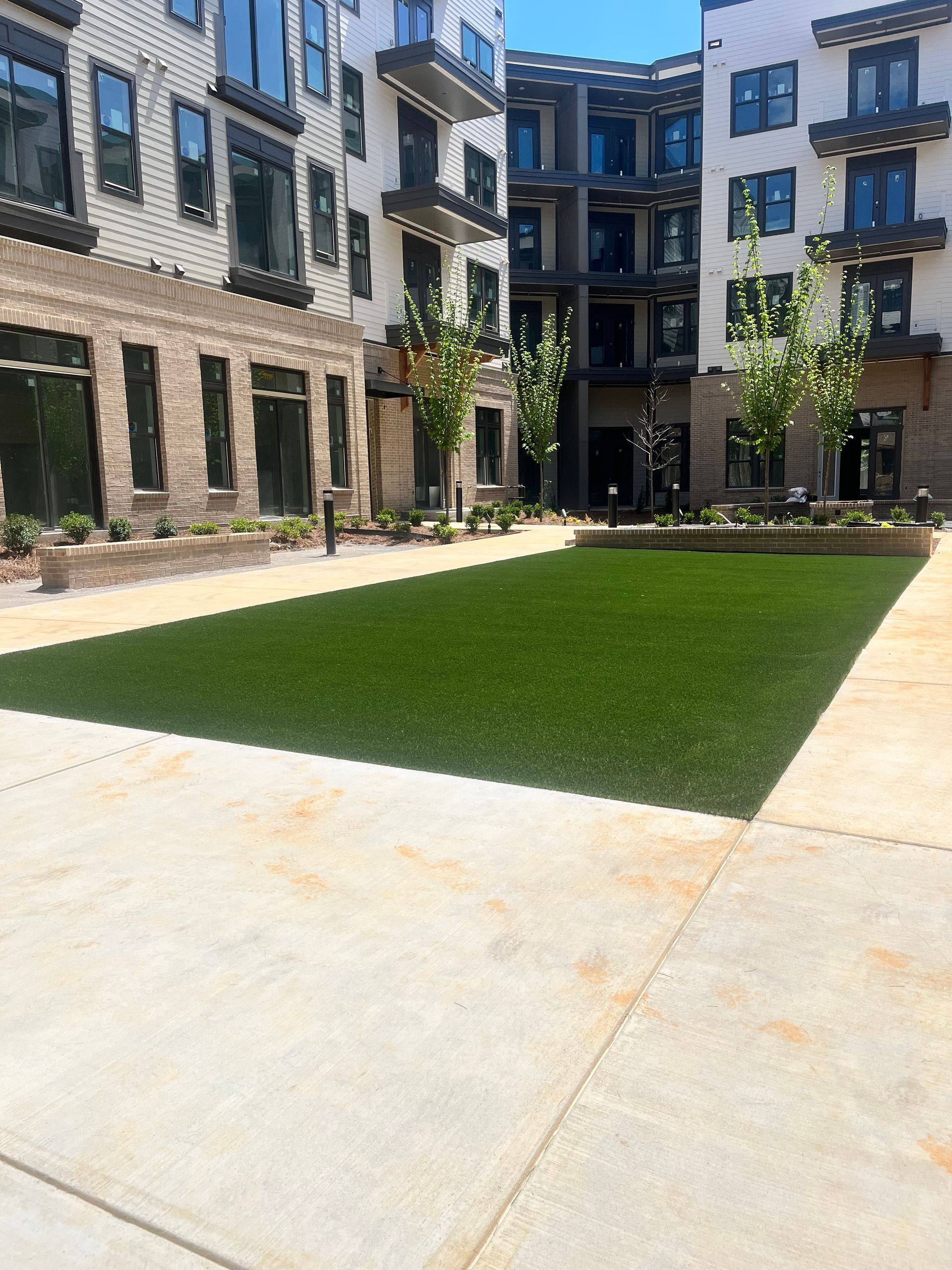 Courtyard with artificial turf, surrounded by multi-story buildings, and concrete walkways.