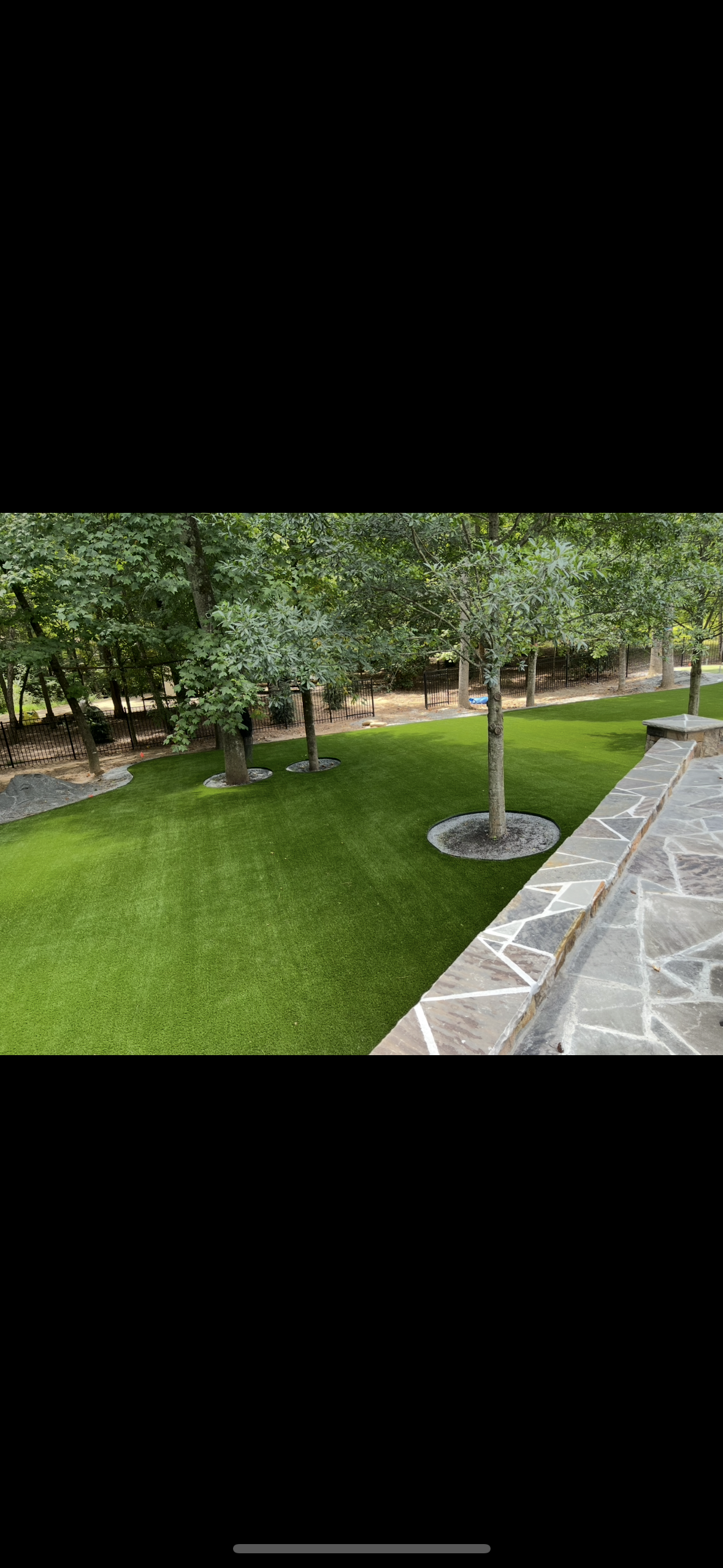 Green lawn with trees in the background, stone patio in the foreground.