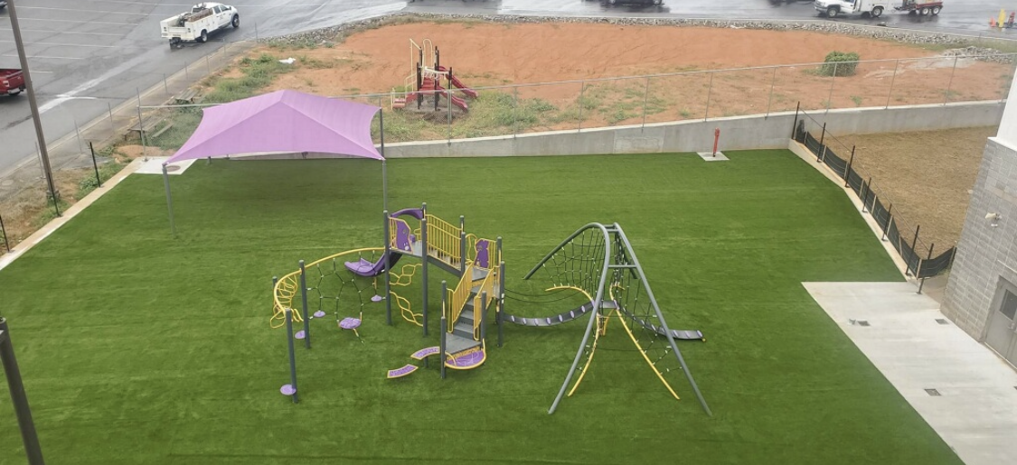 A playground with purple shade structure and green turf, seen from above.