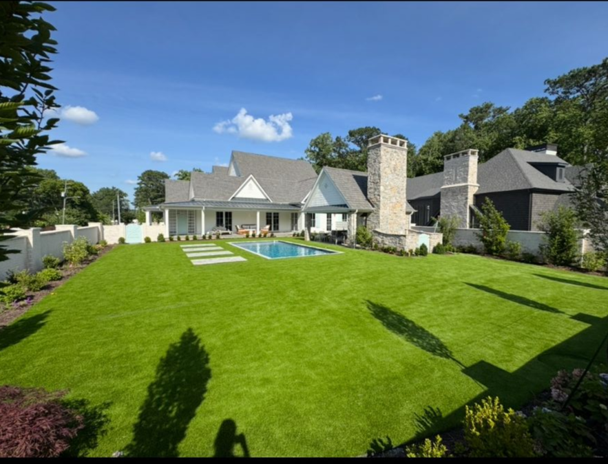 Patio with stone pavers, fire pit, and seating overlooking a green lawn and trees.