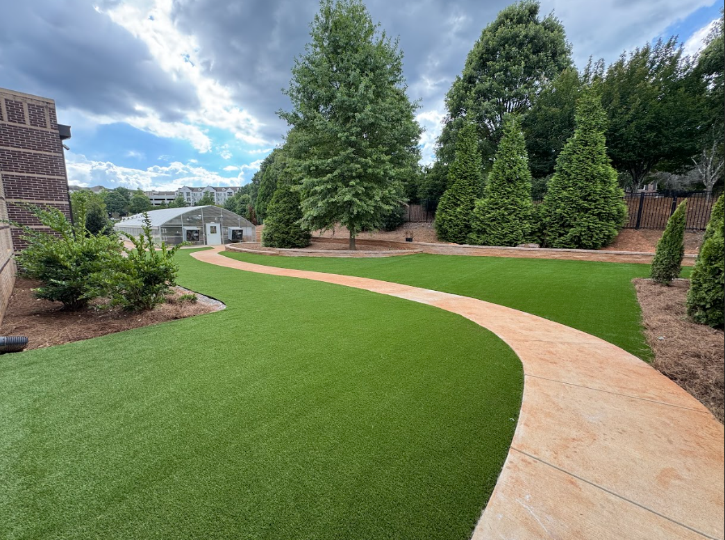 A green lawn in a plaza setting surrounded by buildings and a central gazebo under a partly cloudy sky.
