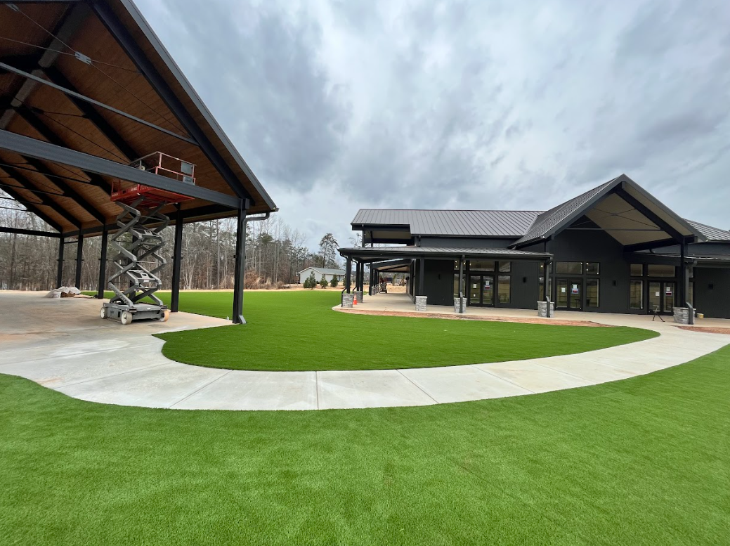 Buildings with a covered pavilion and modern architecture, gray sky, green lawn and a curved walkway.