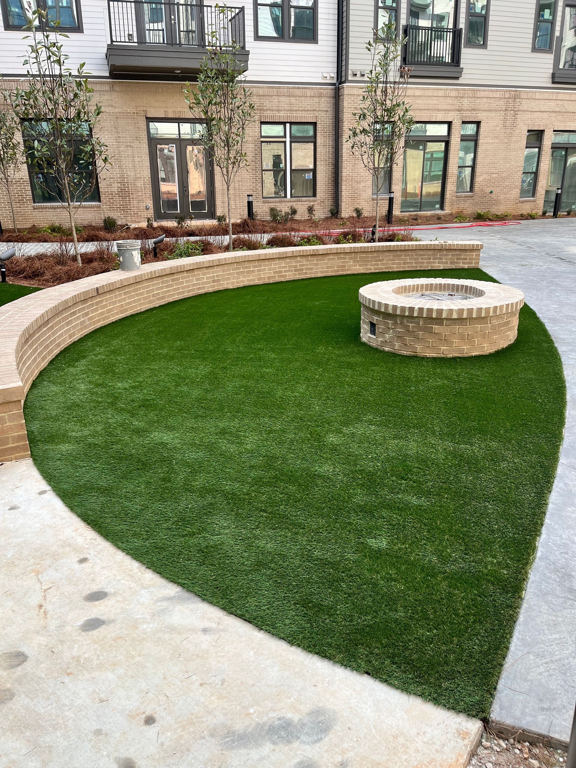 Courtyard with green turf, brick-lined curved wall, and fire pit. Building facade in background.