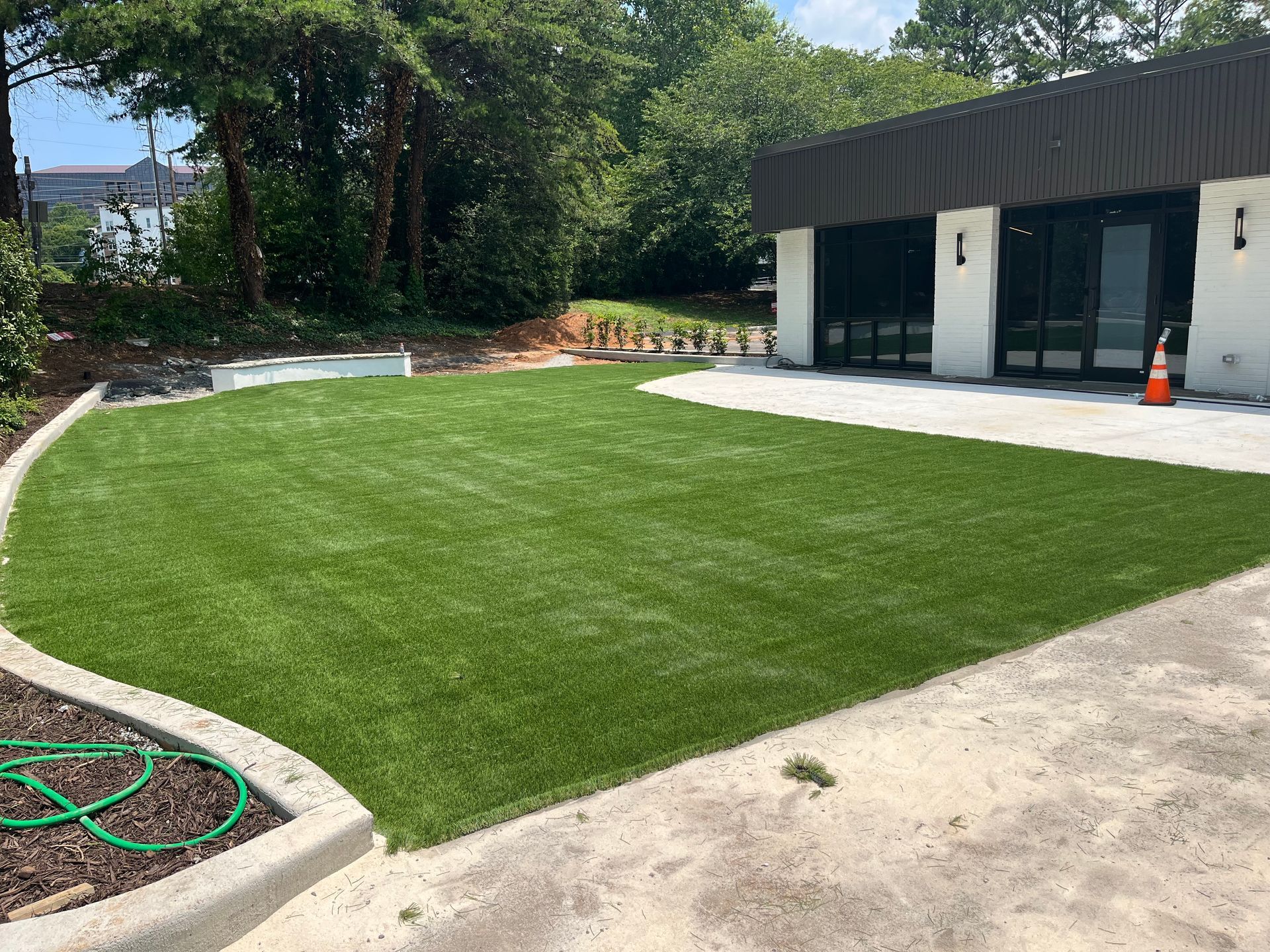 Lush green artificial turf lawn beside a building with dark trim and a concrete patio.