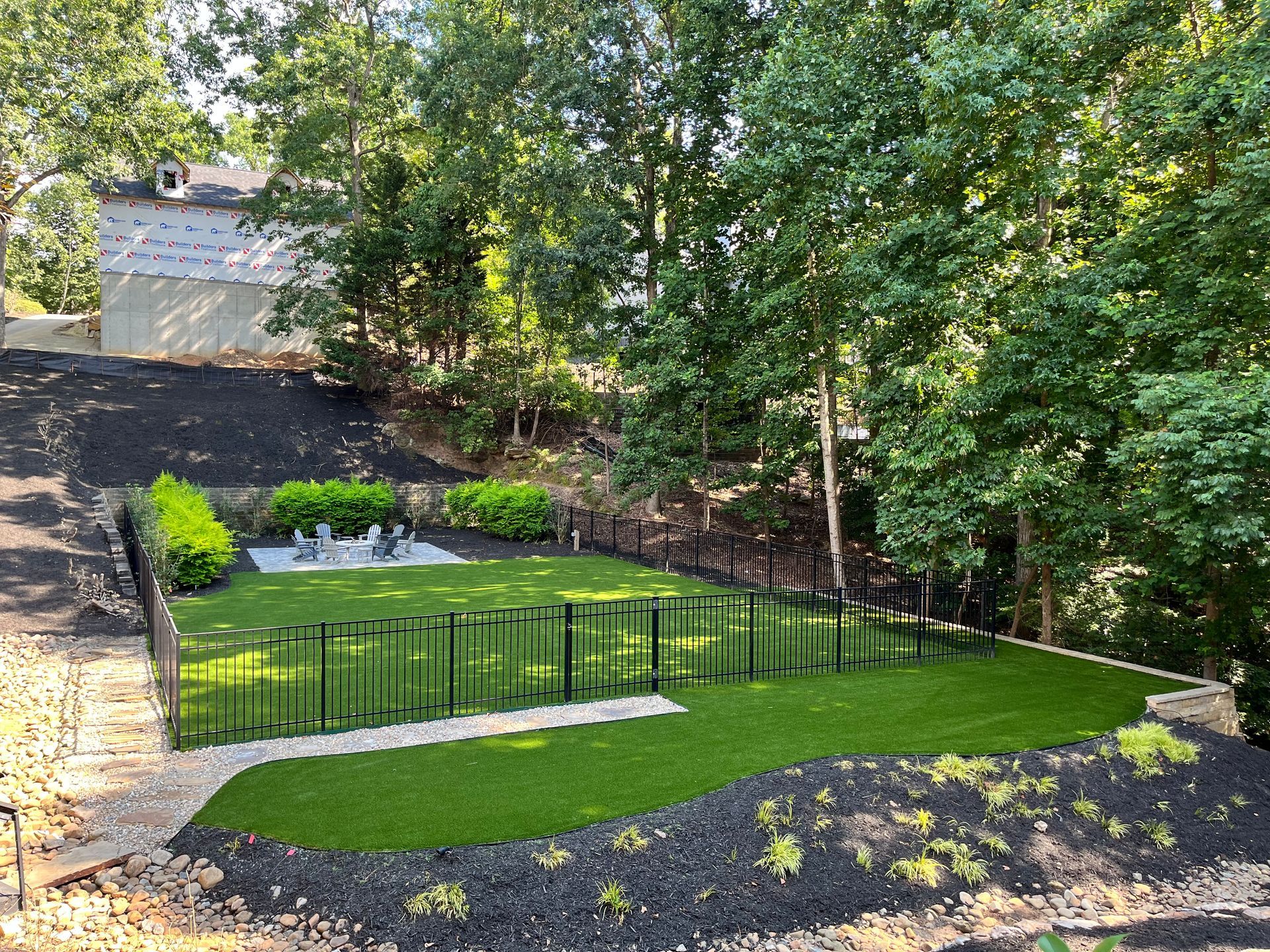 A fenced backyard with green artificial turf, a black fence, and trees, viewed from above.