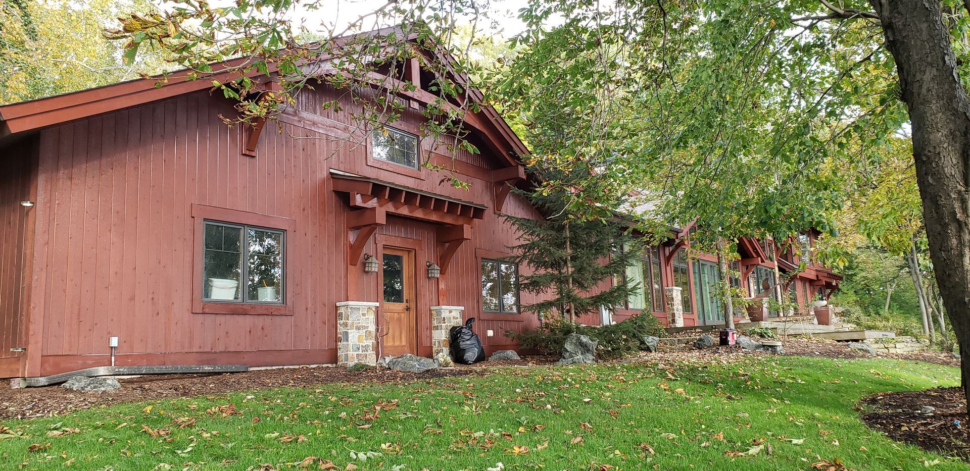 A large red house is sitting in the middle of a lush green field surrounded by trees.