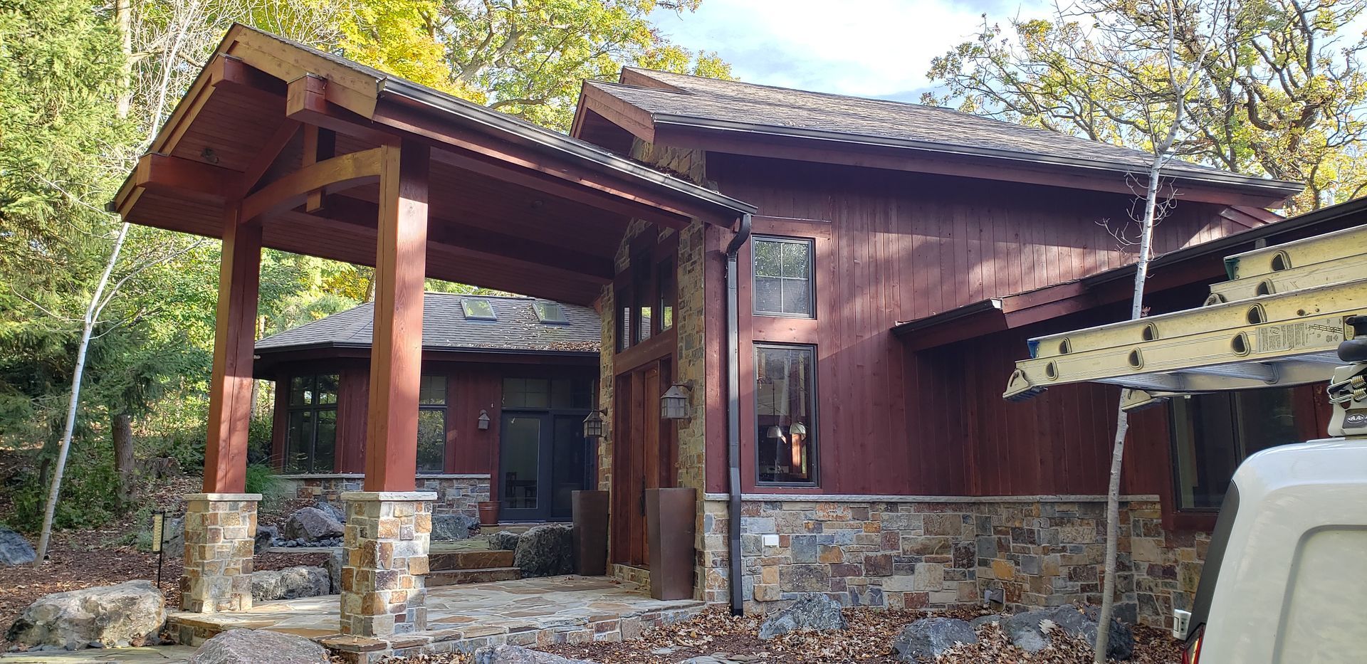 A large red house with a porch and a ladder in front of it.