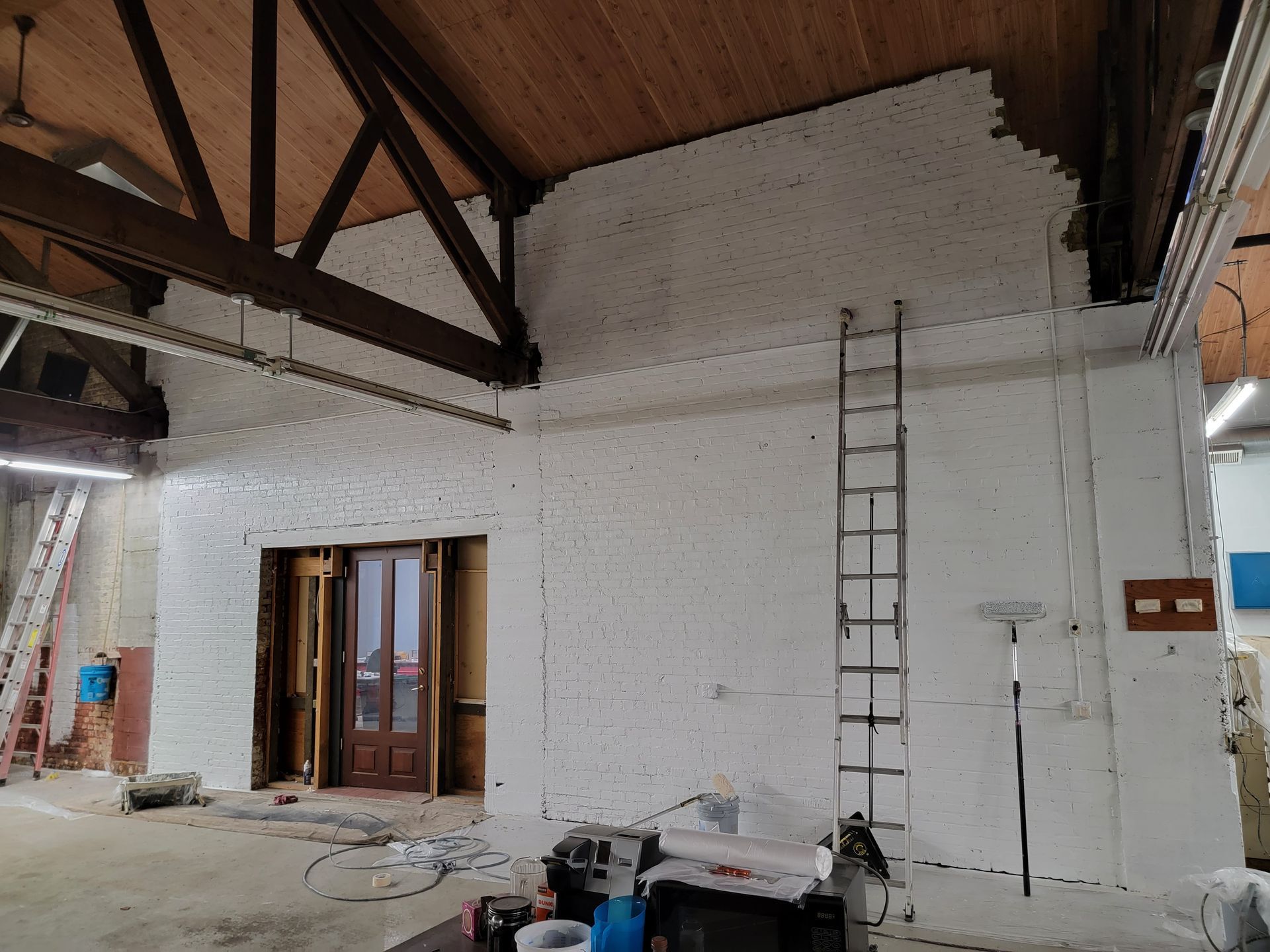 Construction site interior with white walls and exposed wooden beams. A ladder leans against the wall.