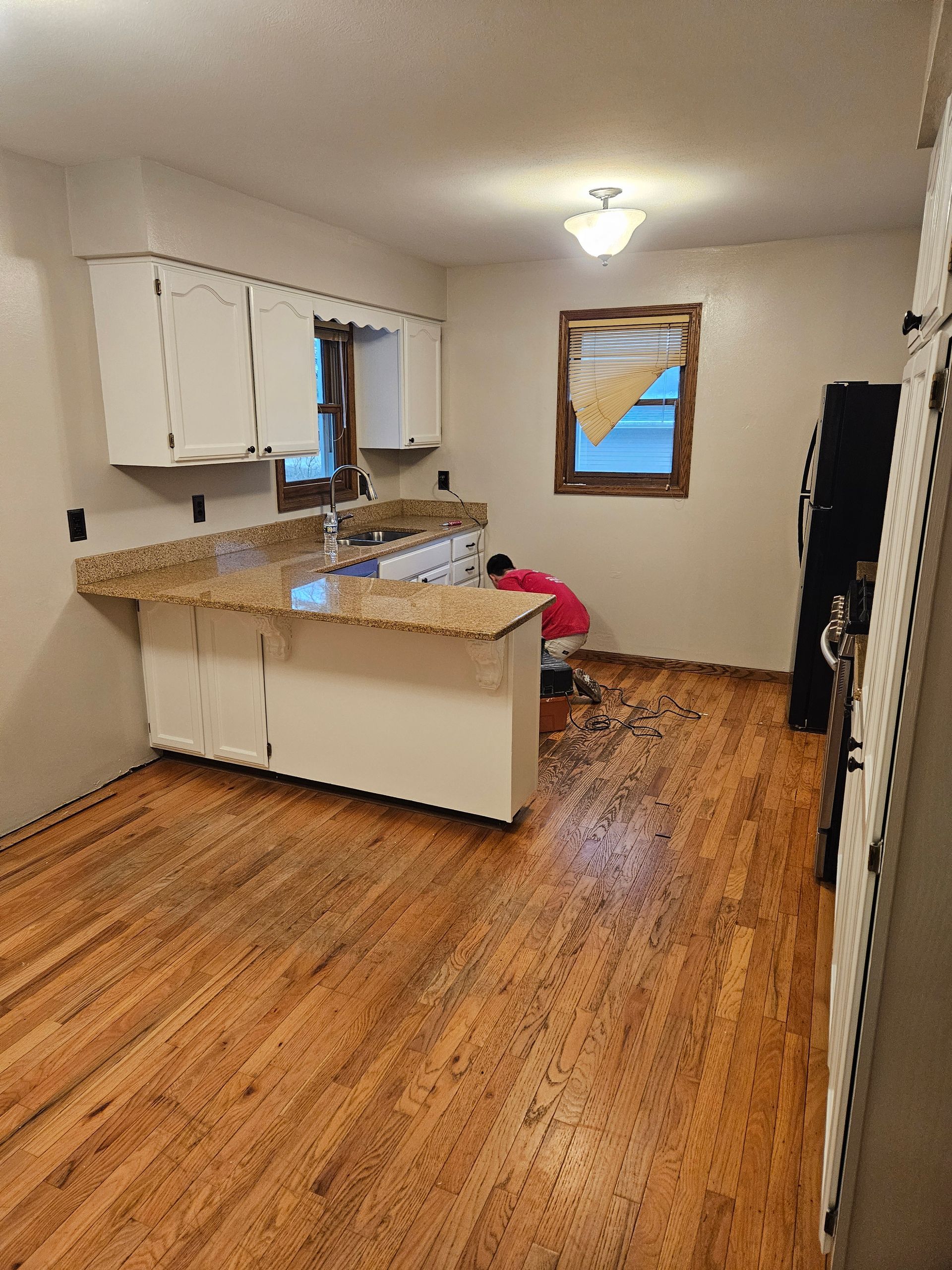 An empty kitchen with hardwood floors and white cabinets