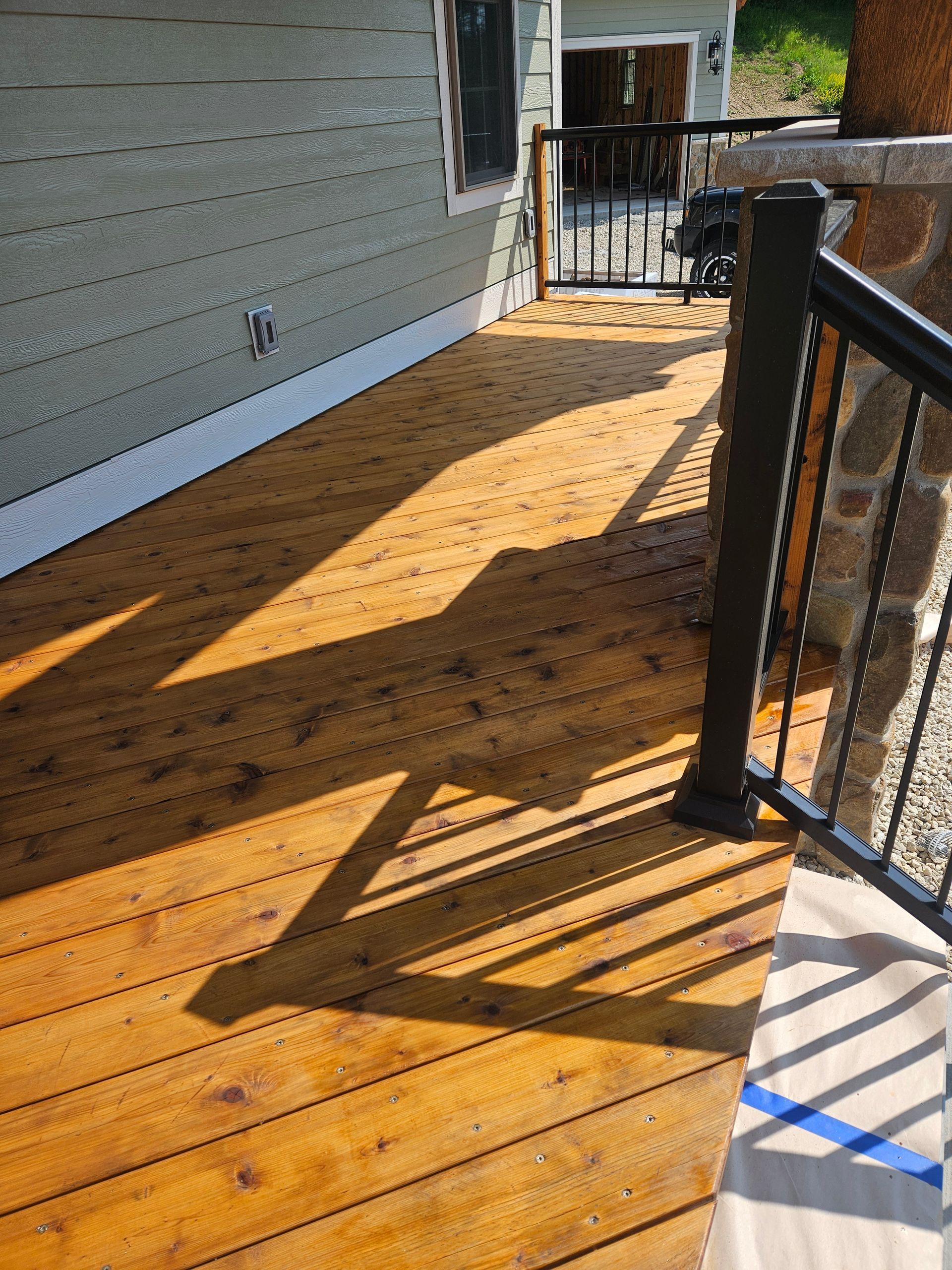 A wooden deck with a black railing and a house in the background