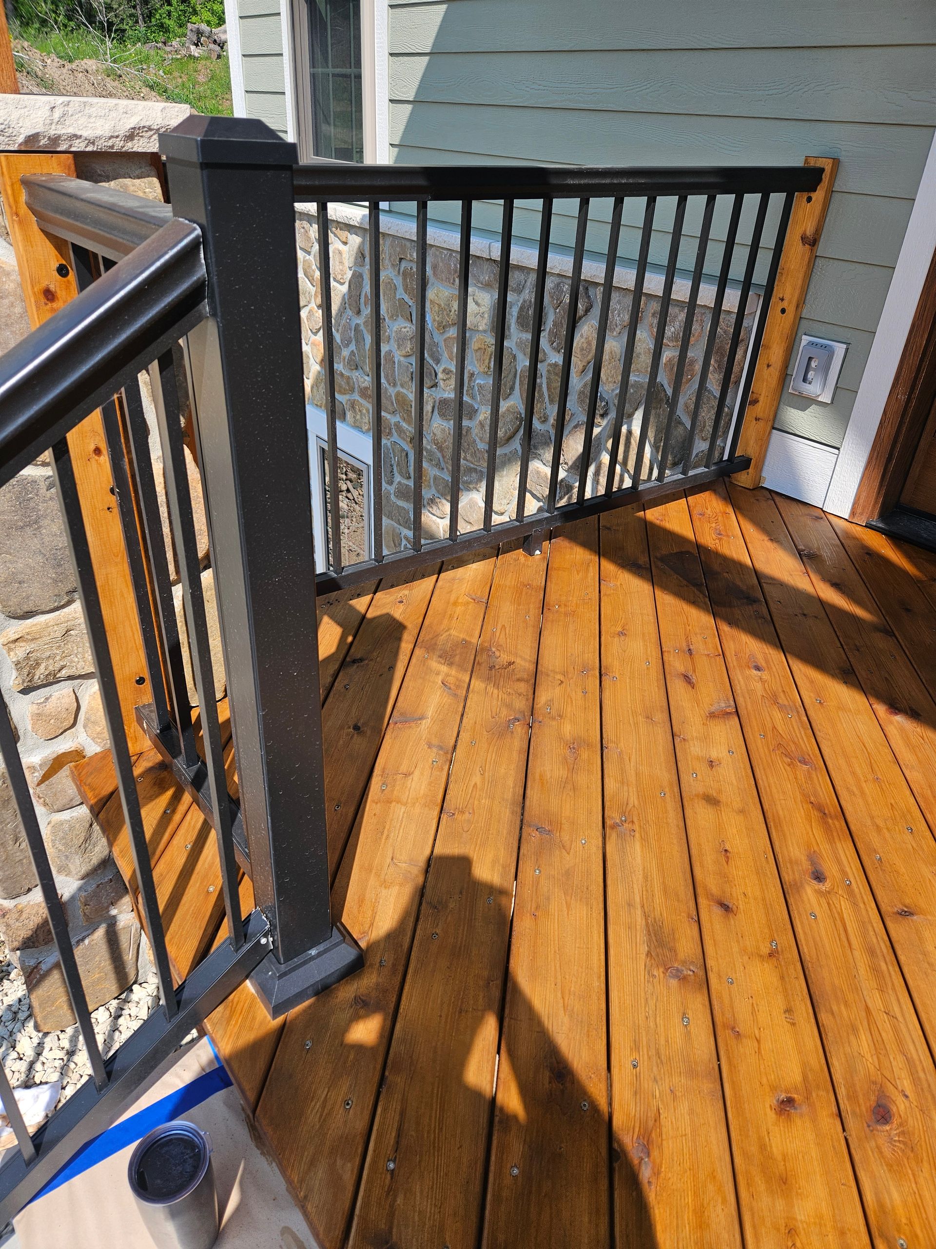 A wooden deck with a black railing is being painted
