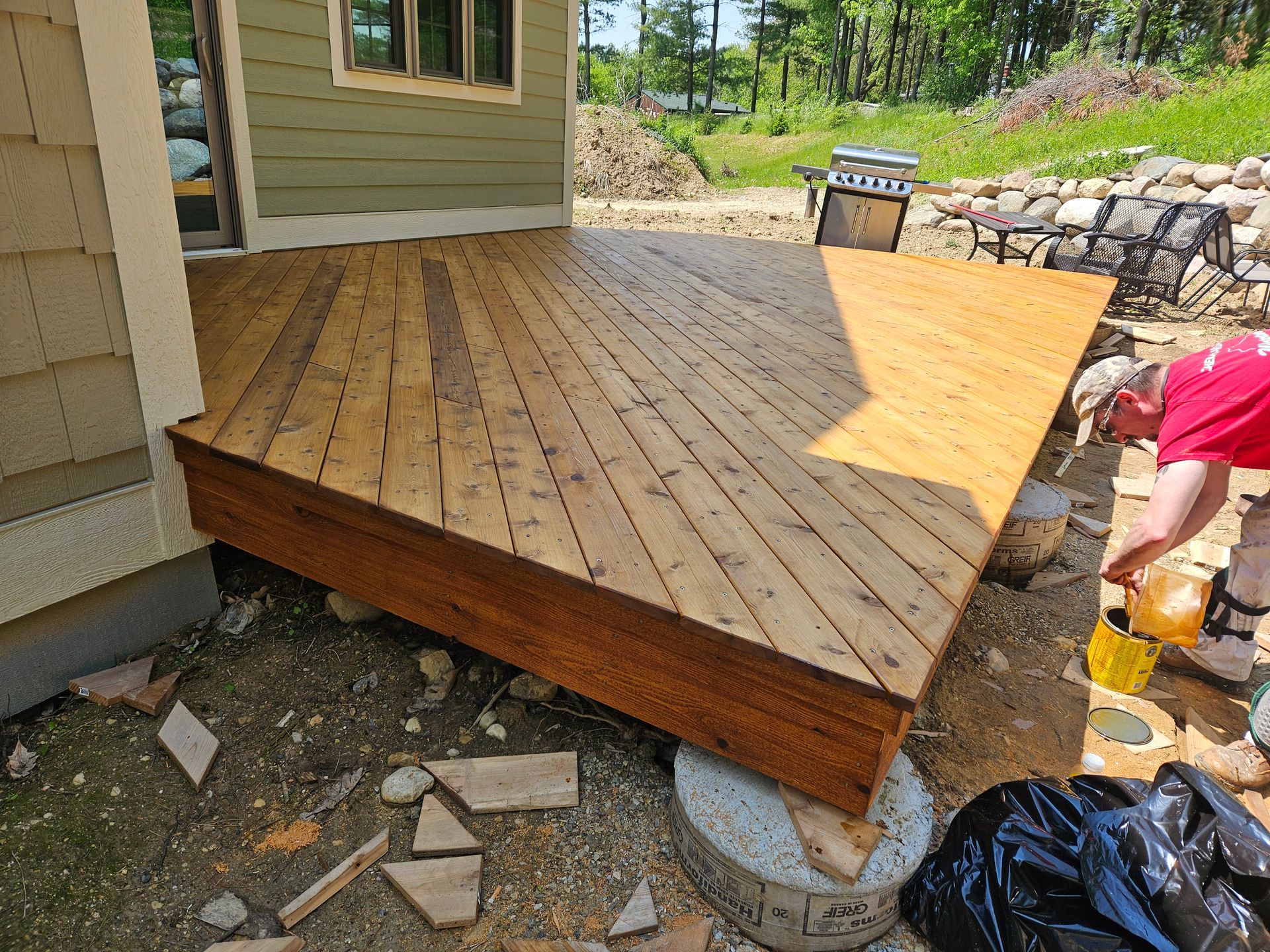 A man is painting a wooden deck in front of a house.