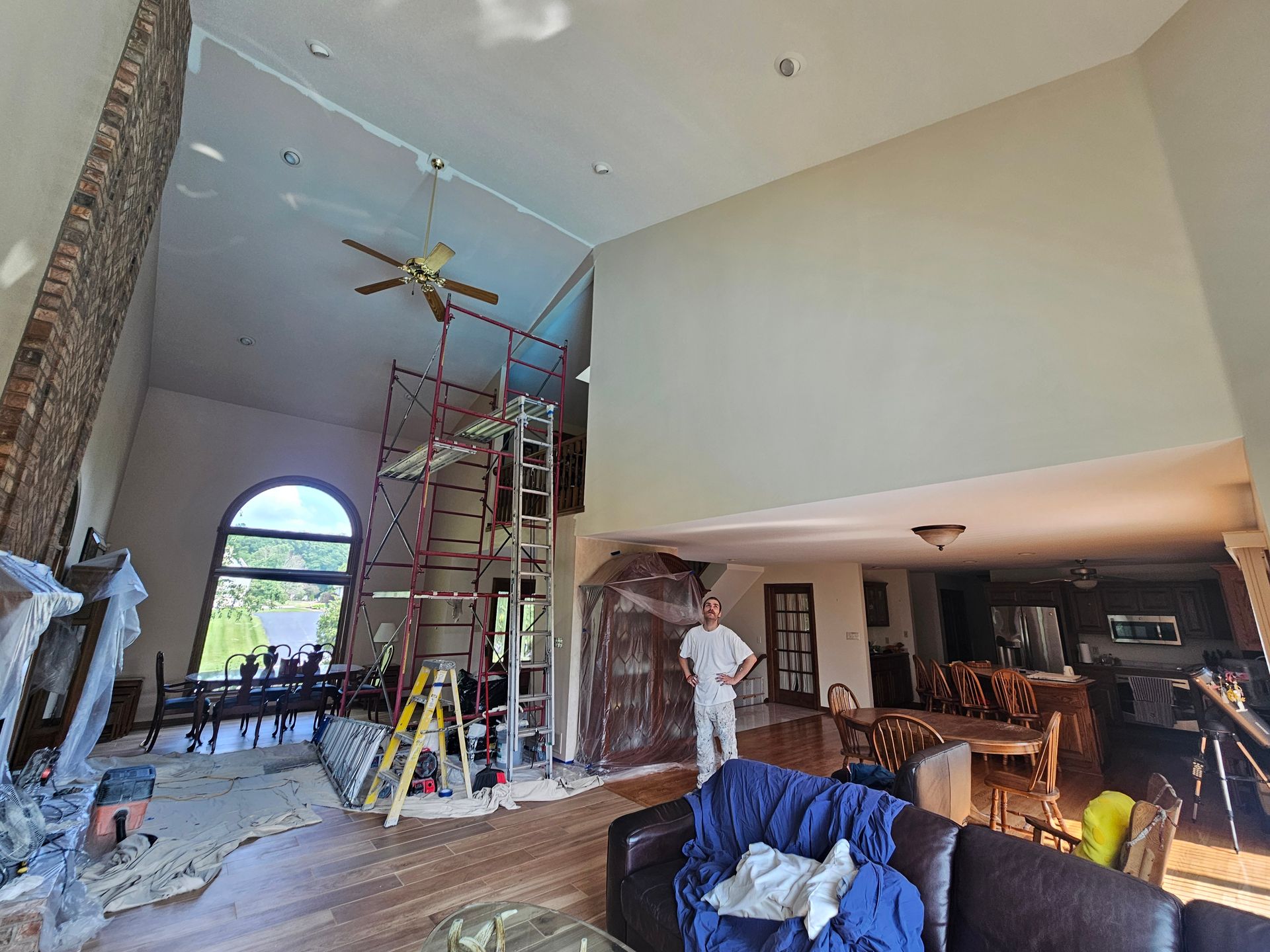 A man is standing in a living room painting a wall.