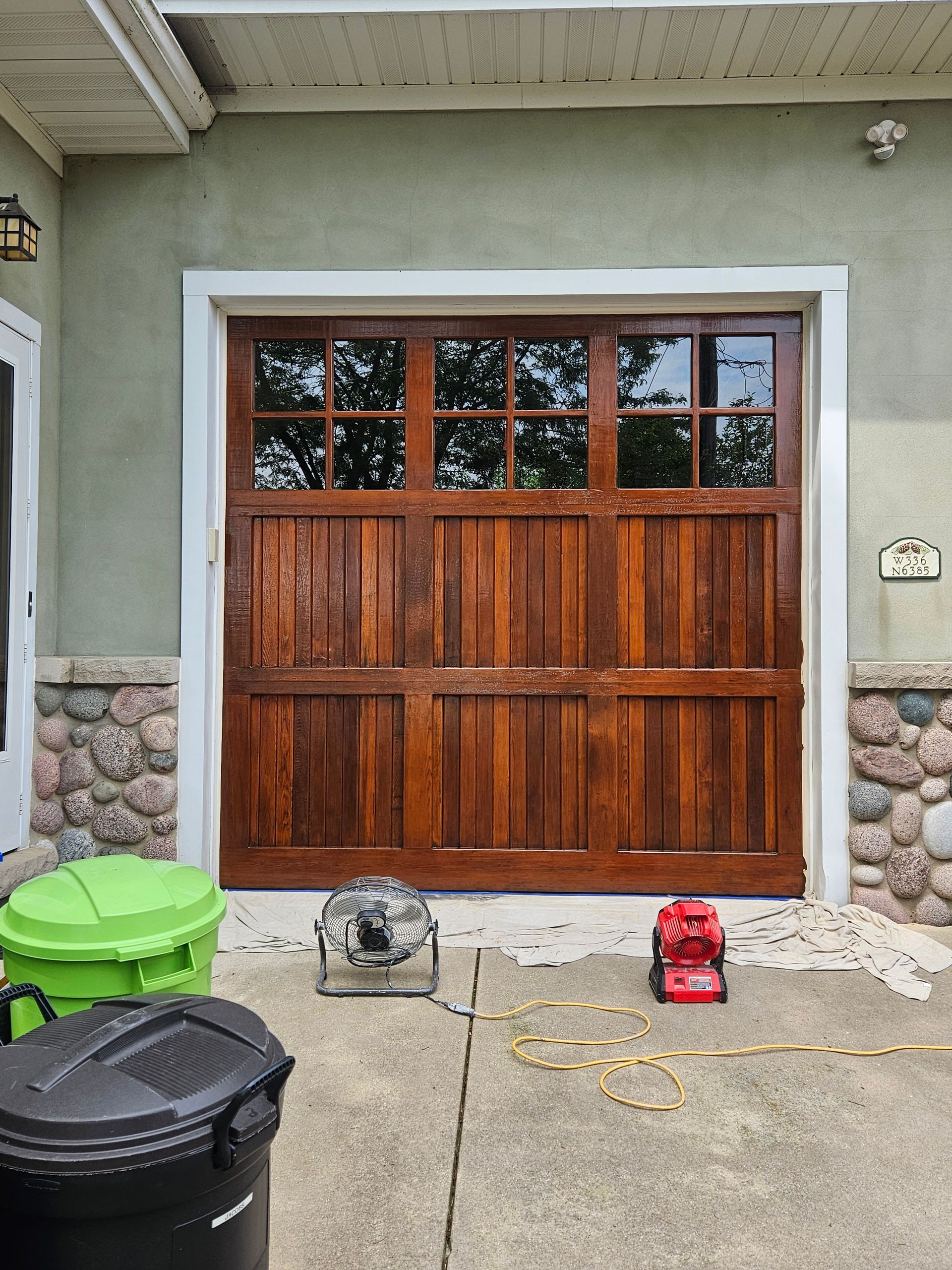 A wooden garage door is being painted in front of a house.