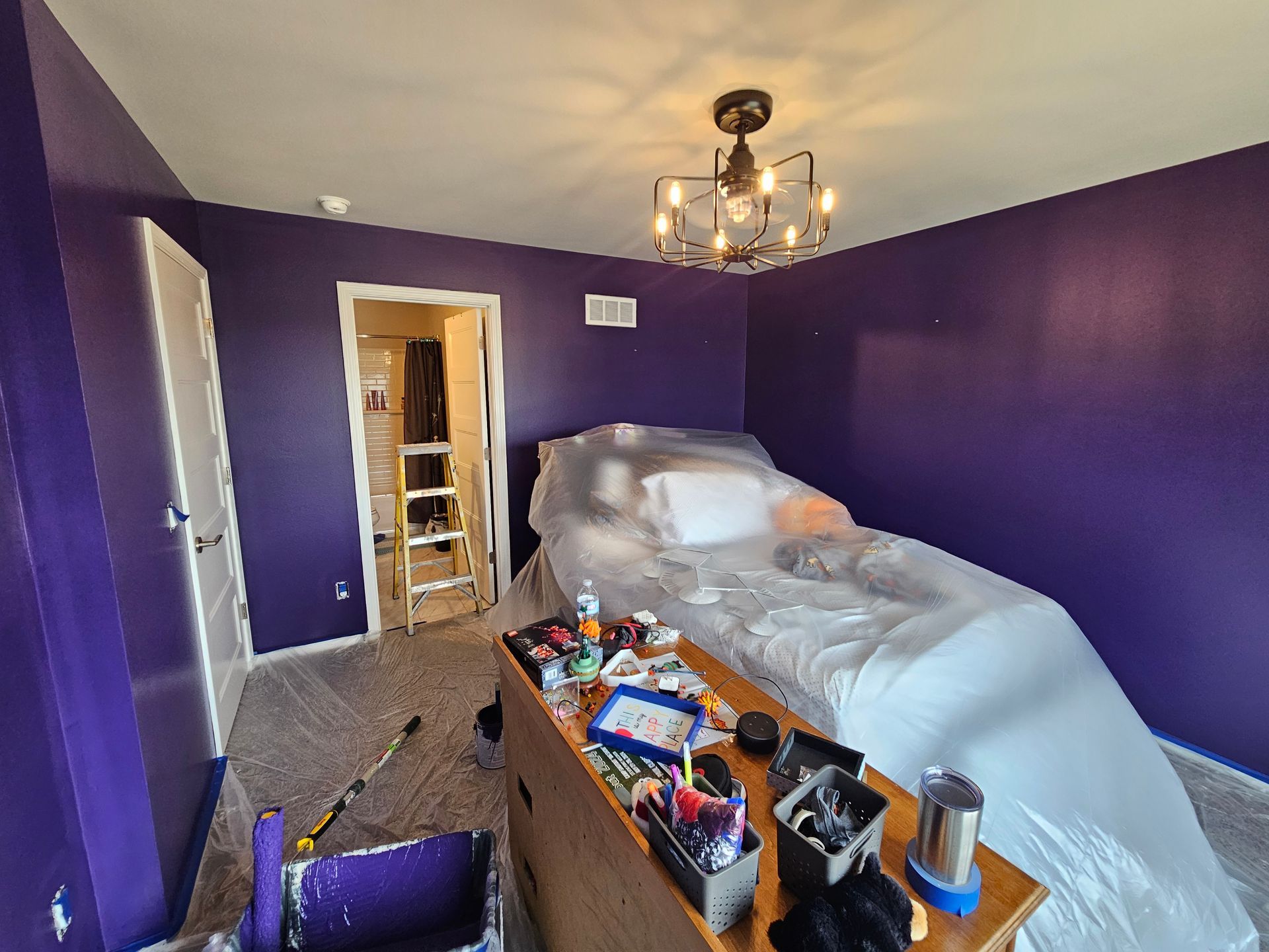 A bedroom with purple walls and a bed covered in plastic.