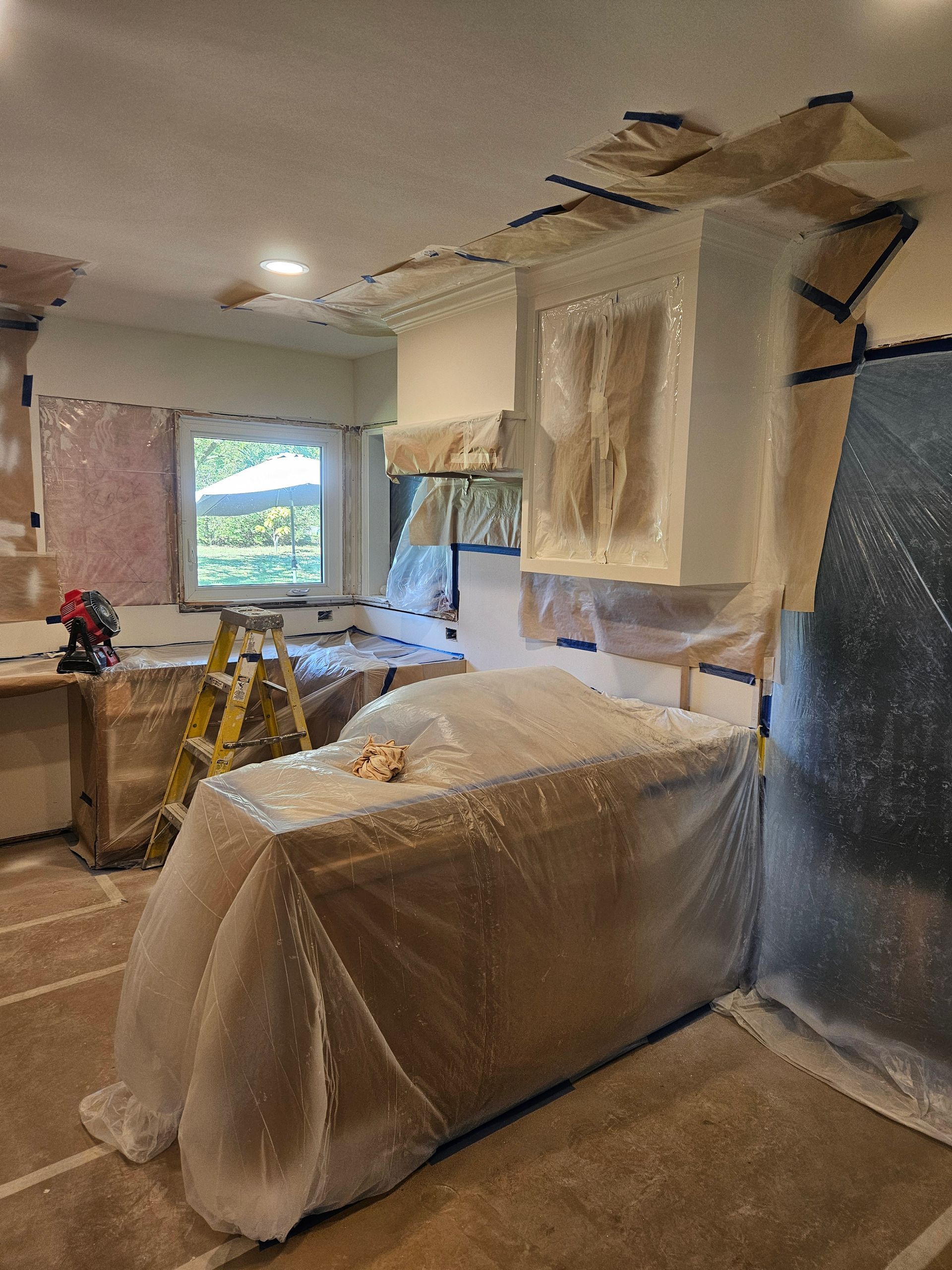 A kitchen is being painted and covered in plastic.