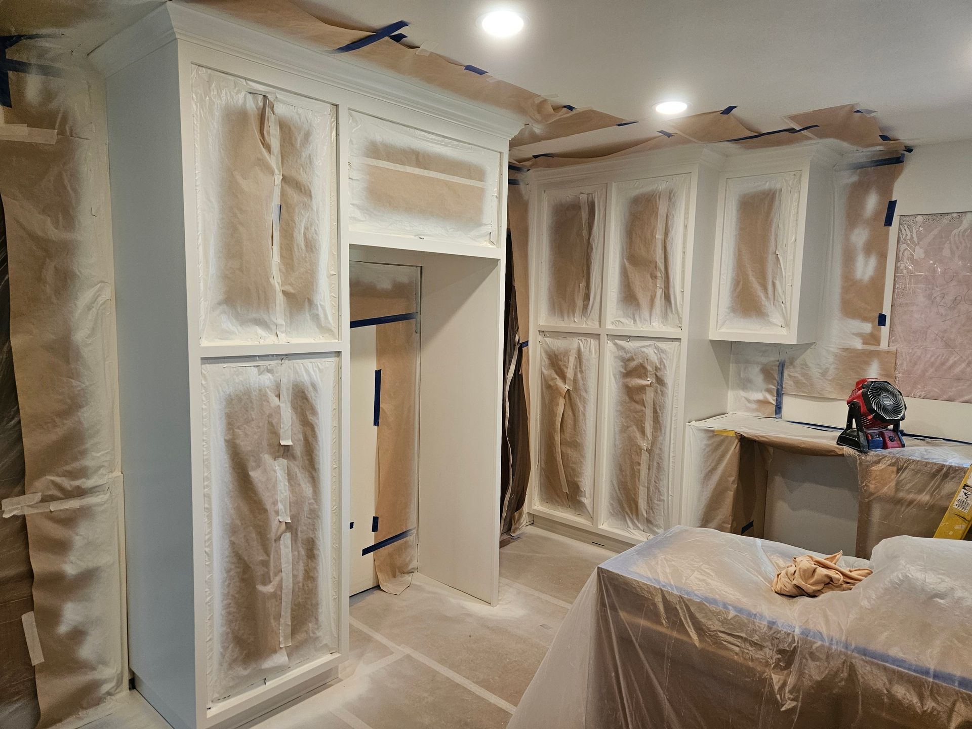 A kitchen is being painted white and covered in plastic.