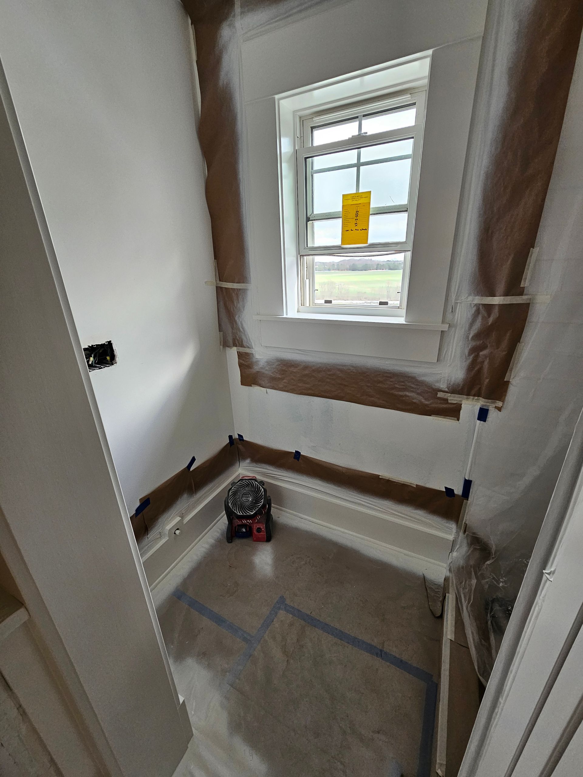 A bathroom with a window and a bathtub covered in plastic.