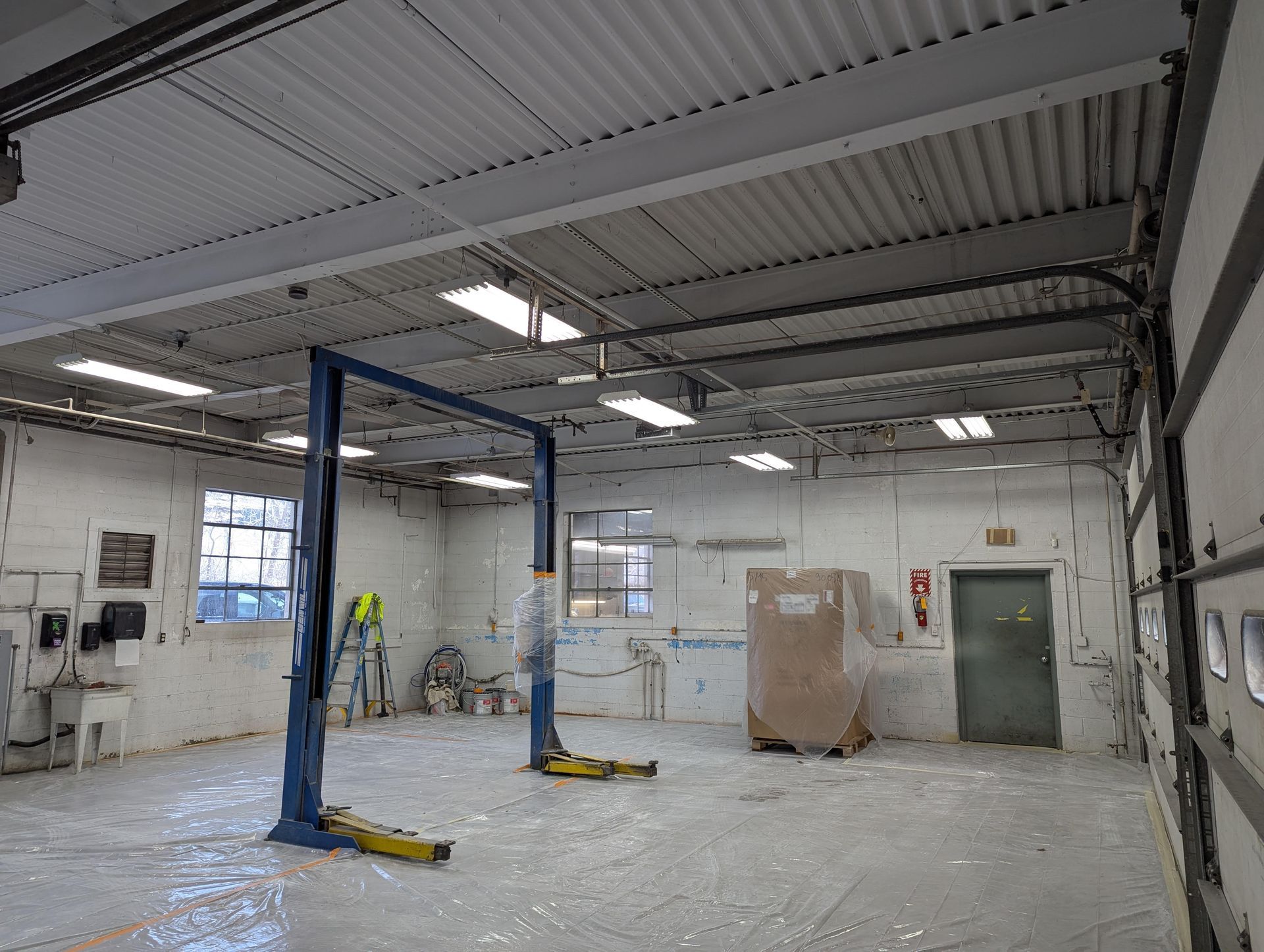 A mechanic's bay with a blue car lift, white walls, and a partially open garage door.