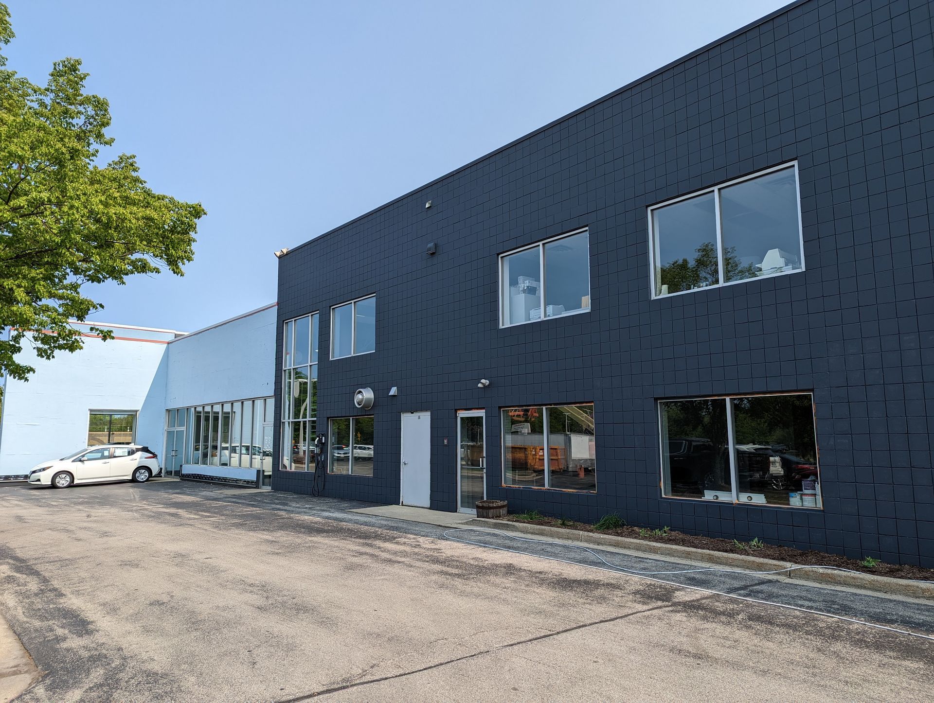 Dark blue and light blue industrial building with a white car parked outside on a sunny day.