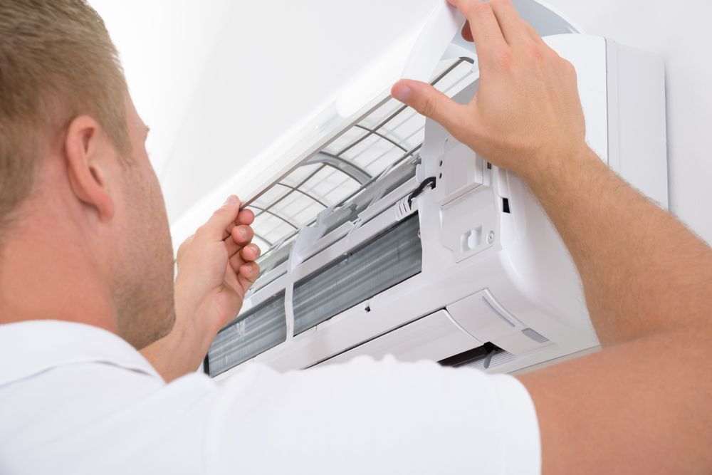 A Man Is Cleaning The Filter Of An Air Conditioner — East Coast Air In Cessnock, NSW