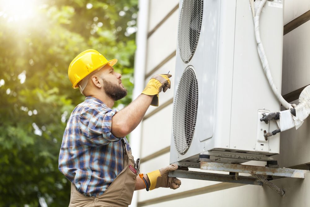 A Man Is Installing An Air Conditioner On The Side Of A Building — East Coast Air In Cessnock, NSW