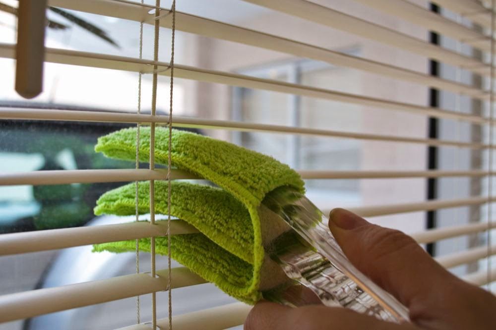 Uma pessoa está limpando persianas com uma escova verde.